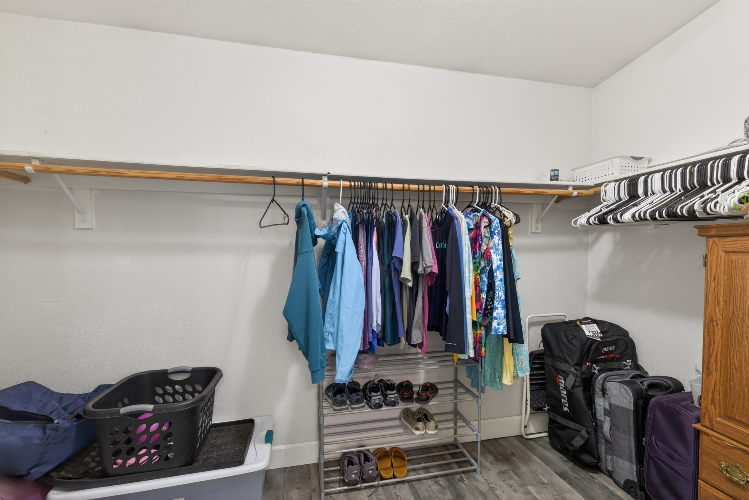 Walk-in closet featuring wood-finish flooring, two levels of hanging rods, and a white color palette