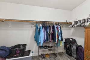 Walk-in closet featuring wood-finish flooring, two levels of hanging rods, and a white color palette