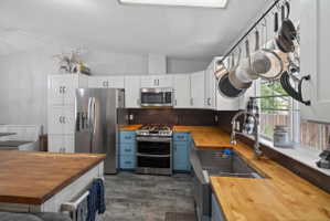 Modern kitchen featuring light wood-finish countertops, white cabinetry, stainless steel appliances, a deep basin sink with a gooseneck faucet, and light gray wood-finish flooring