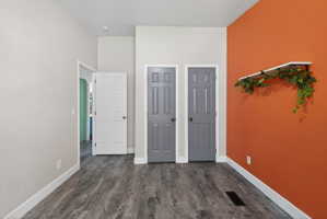 Spacious room featuring wood-finish flooring, white baseboards, and a distinctive orange accent wall