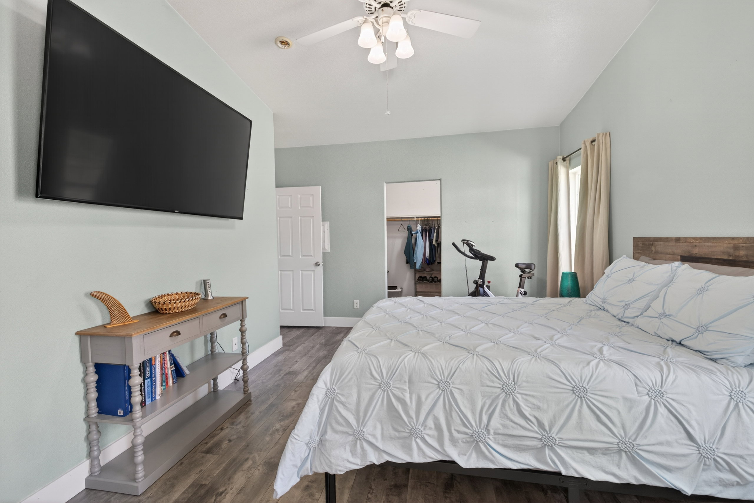 Room featuring wood-finish flooring, light blue wall paint, a built-in closet with shelving and hanging space, a window with curtains, and a ceiling fan