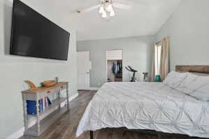 Room featuring wood-finish flooring, light blue wall paint, a built-in closet with shelving and hanging space, a window with curtains, and a ceiling fan