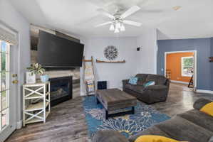 Living area with wood-finish flooring, a ceiling fan, and a fireplace featuring a wood-panel accent wall