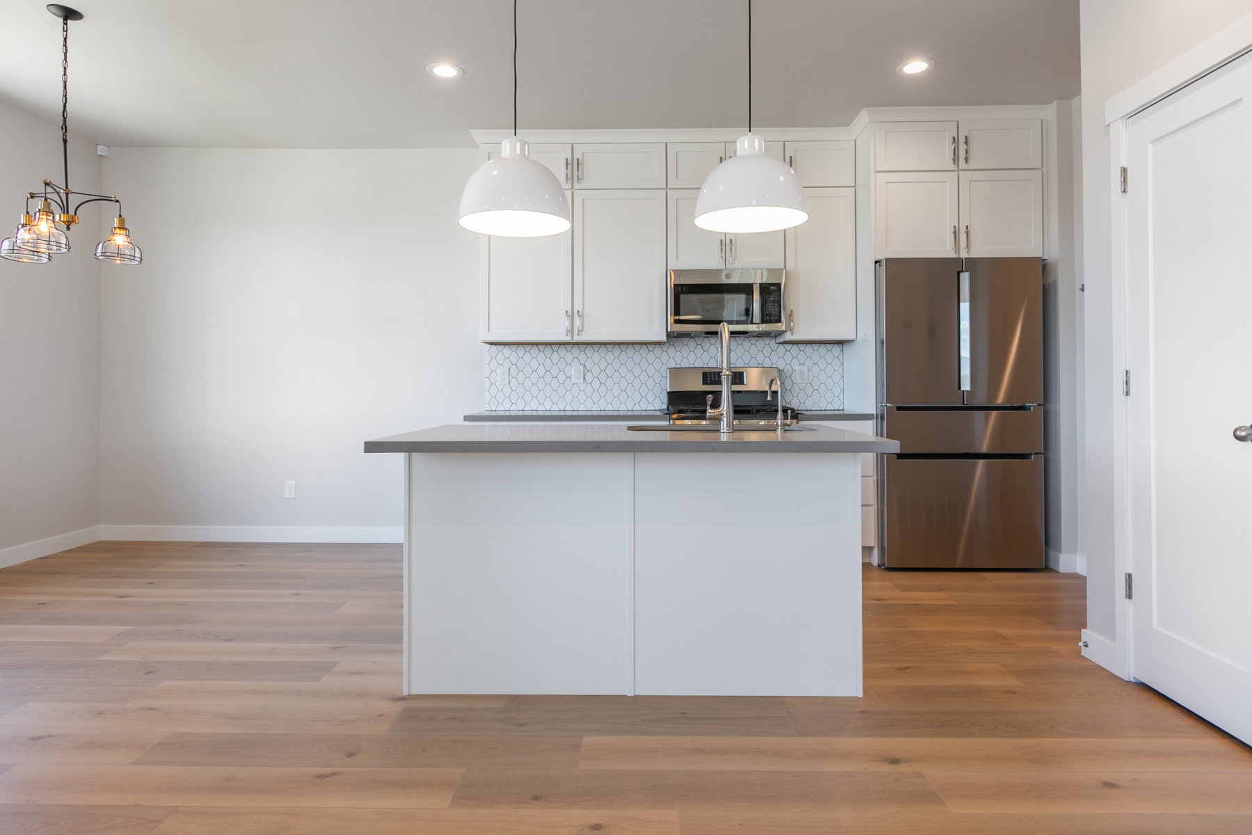 Contemporary kitchen featuring a central island with a sink, stainless steel appliances, white cabinetry, and a geometric tile backsplash