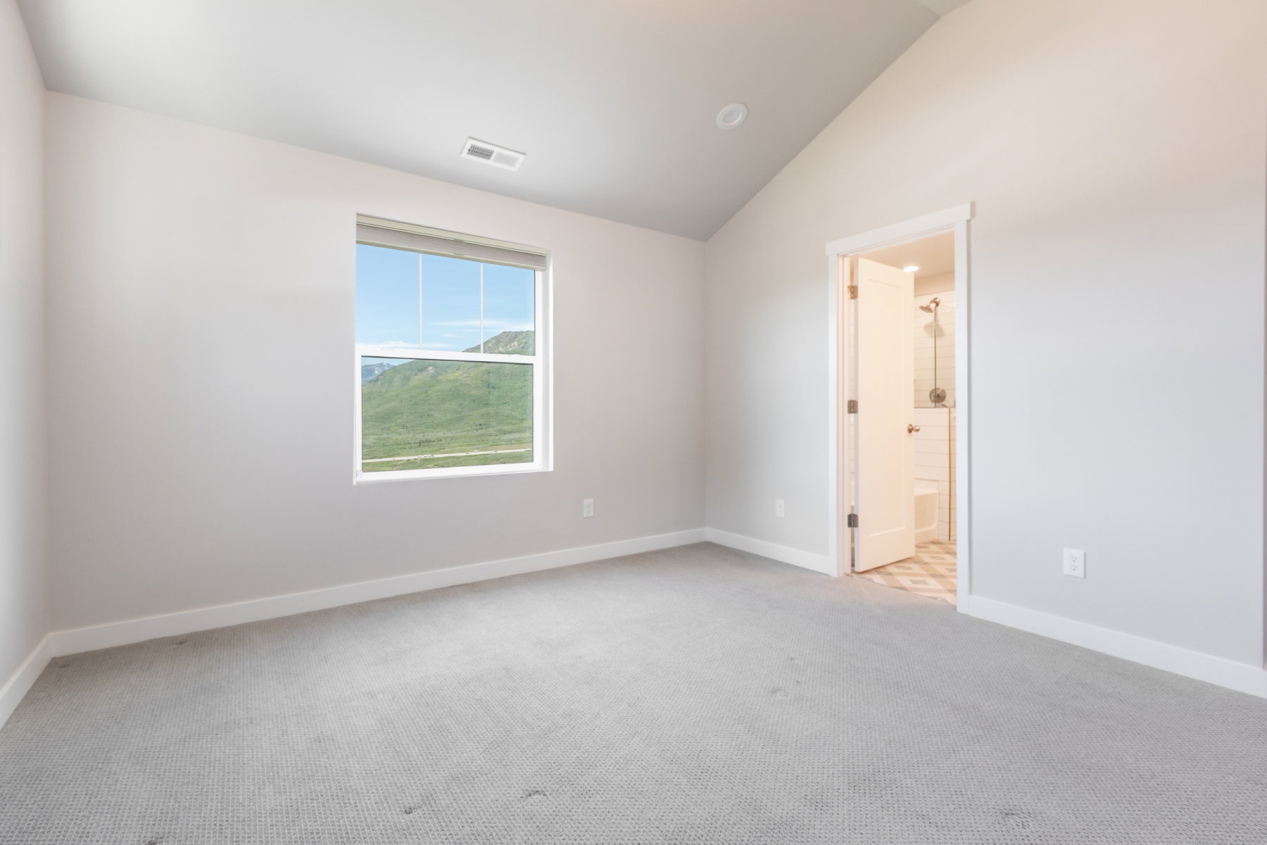 Carpeted room with a vaulted ceiling, a large window, and an en-suite bathroom featuring a shower with white subway tile