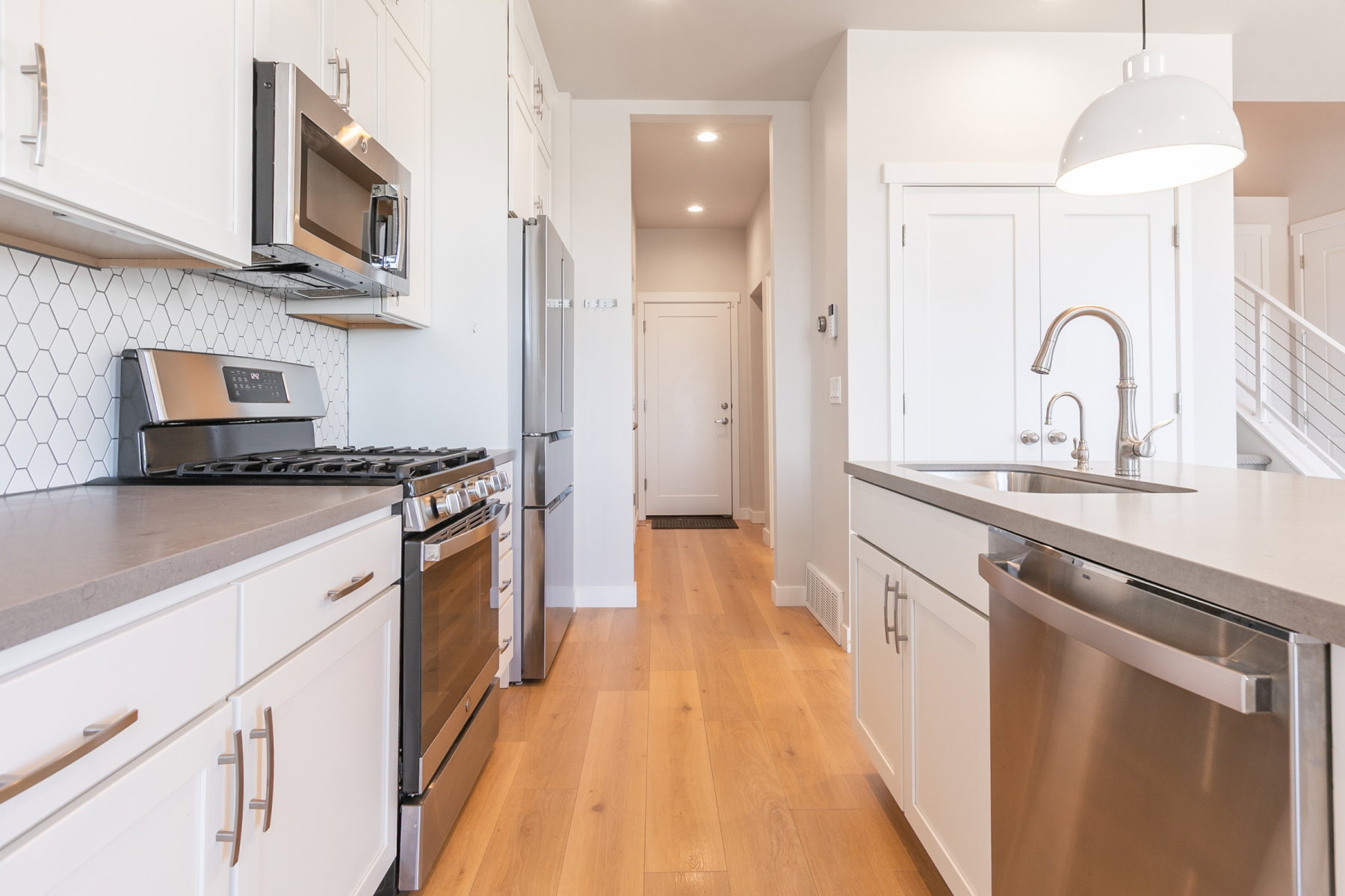 Modern kitchen featuring white cabinetry, stainless steel appliances, light wood-finish flooring, a contemporary hexagonal tile backsplash, and stone countertops