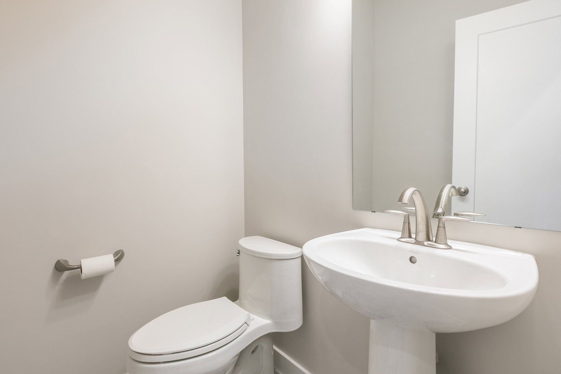 Bright bathroom featuring a pedestal sink with brushed nickel fixtures, a framed mirror, and a modern toilet