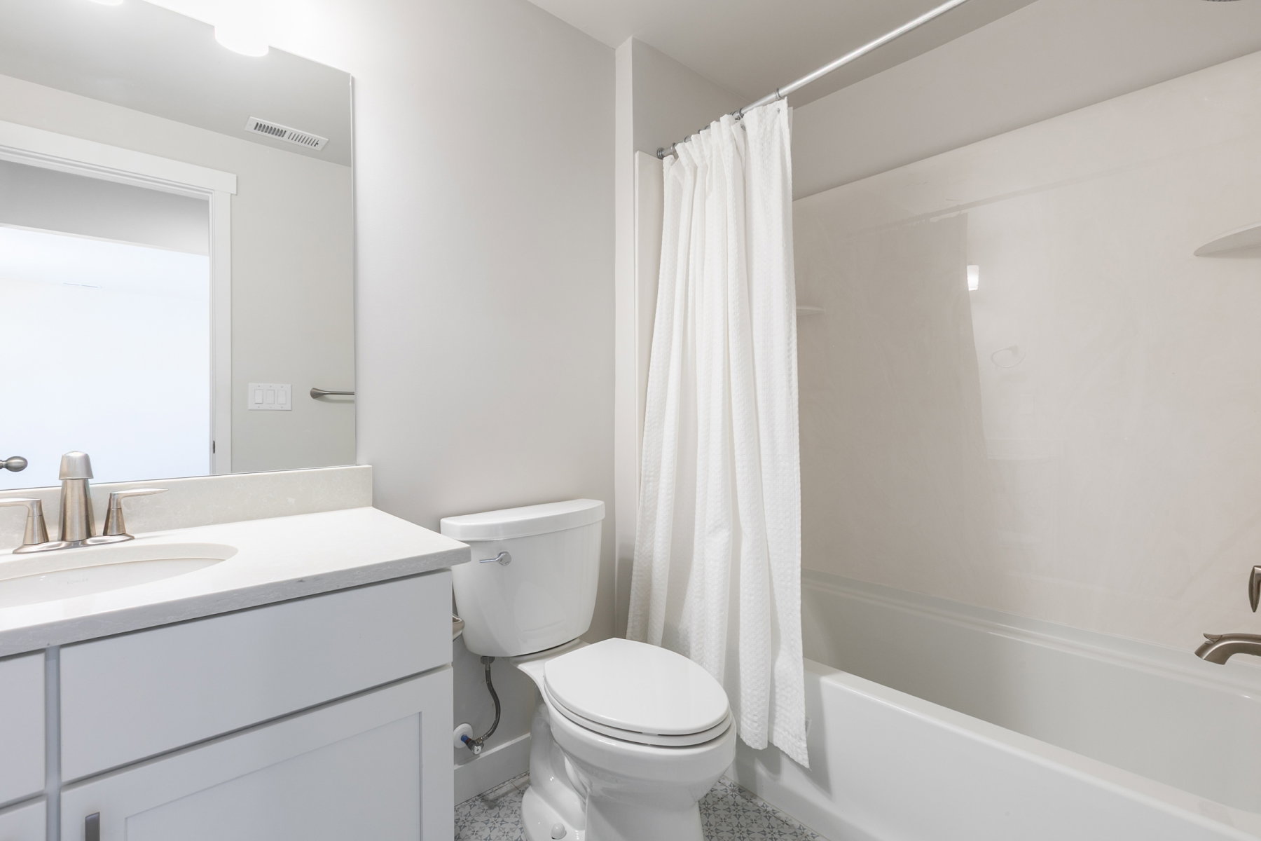 Bathroom featuring a white vanity with a light-toned countertop, an undermount sink with a brushed nickel faucet, a toilet, a full-size mirror, and a white shower/tub combination