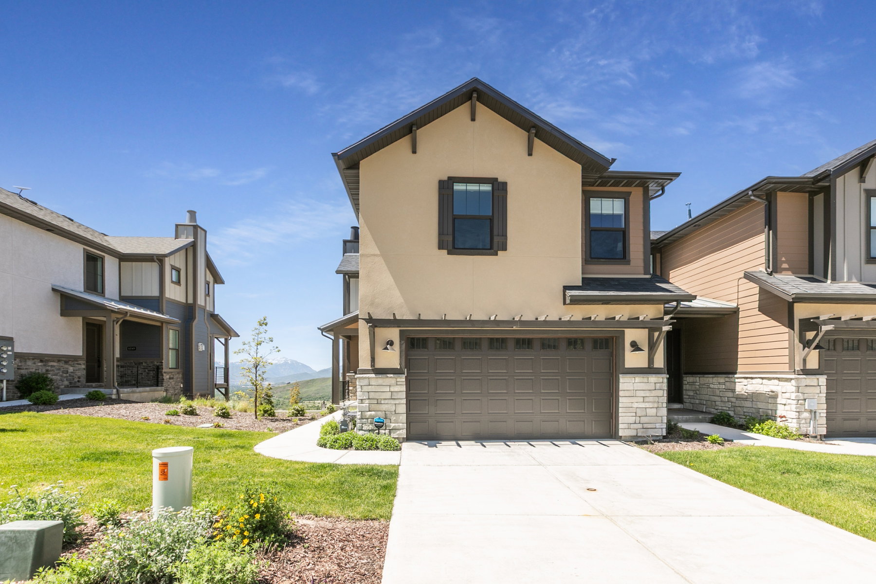 Contemporary stucco exterior featuring a two-car garage, stone veneer accents, dark window shutters, and a concrete driveway