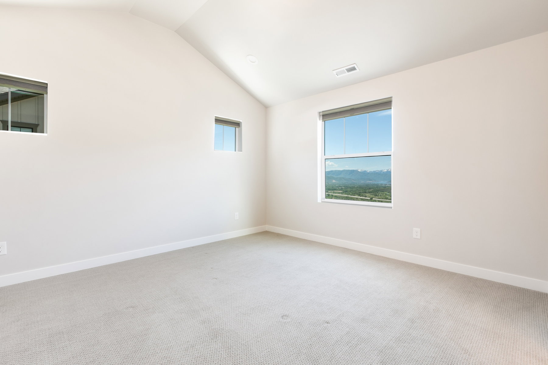 Spacious room featuring vaulted ceilings, a large window with mountain scenery, two additional windows, and light-toned carpeting