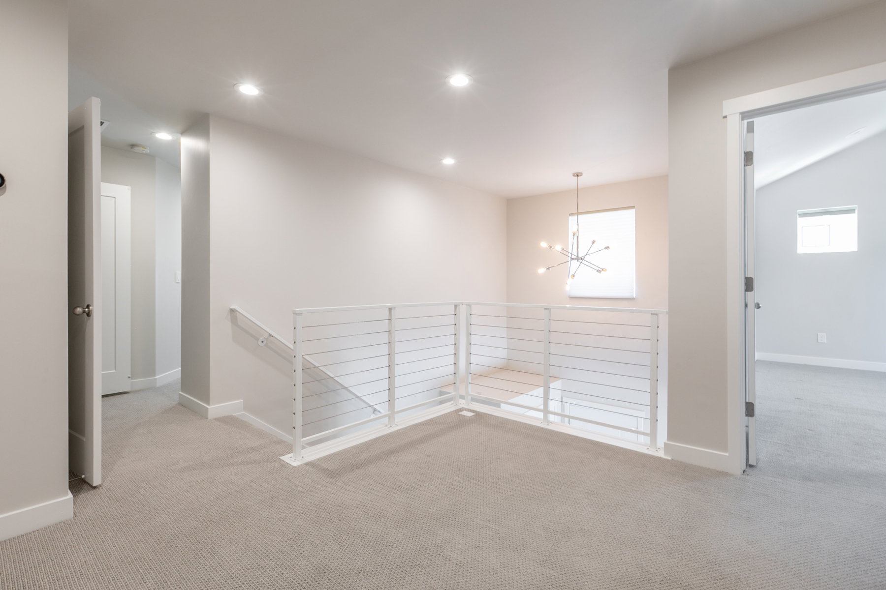 Upper-level landing featuring a modern cable railing system and recessed lighting