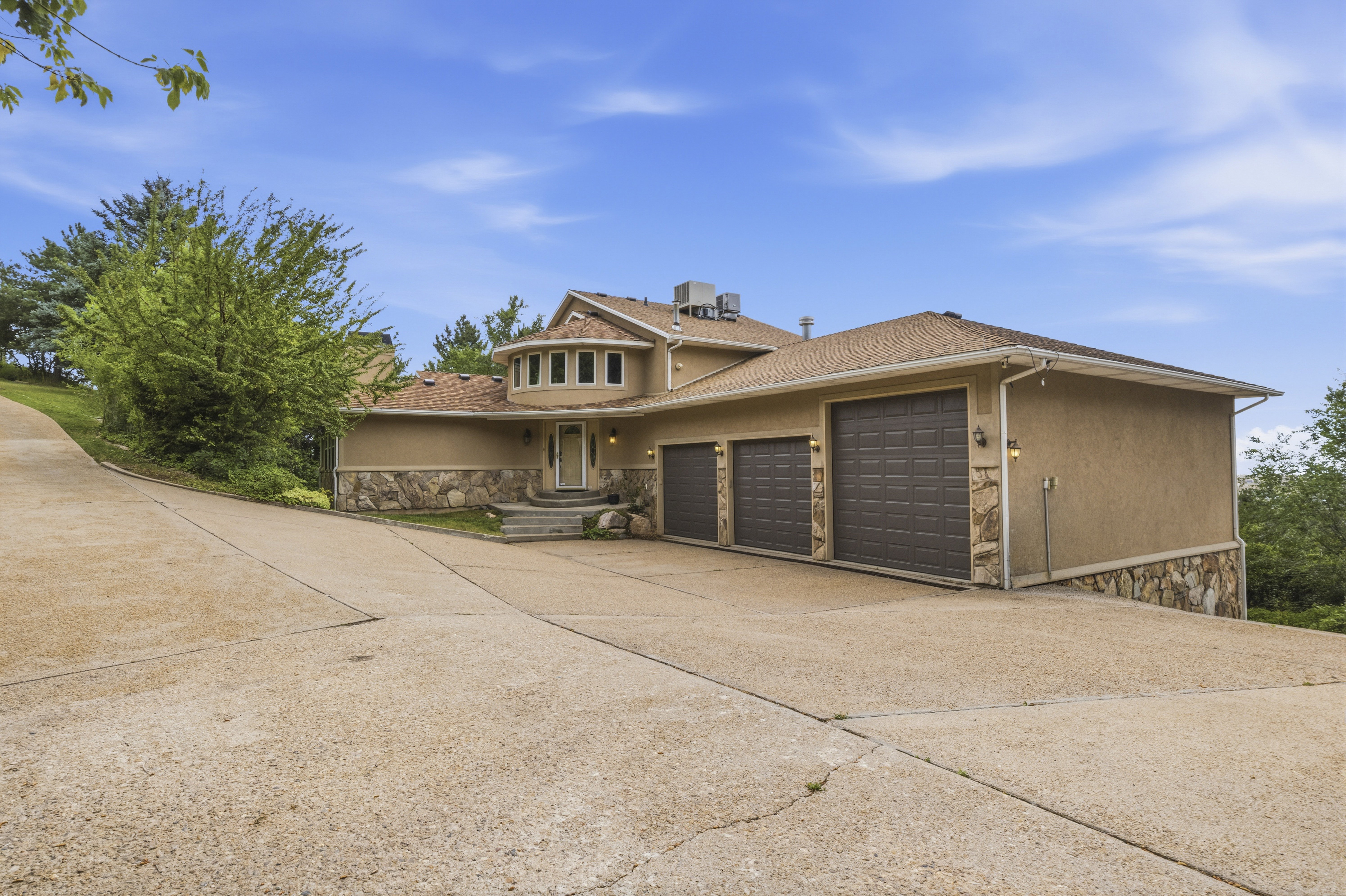 Stucco exterior with stone accents, a multi-car garage, and a curved driveway