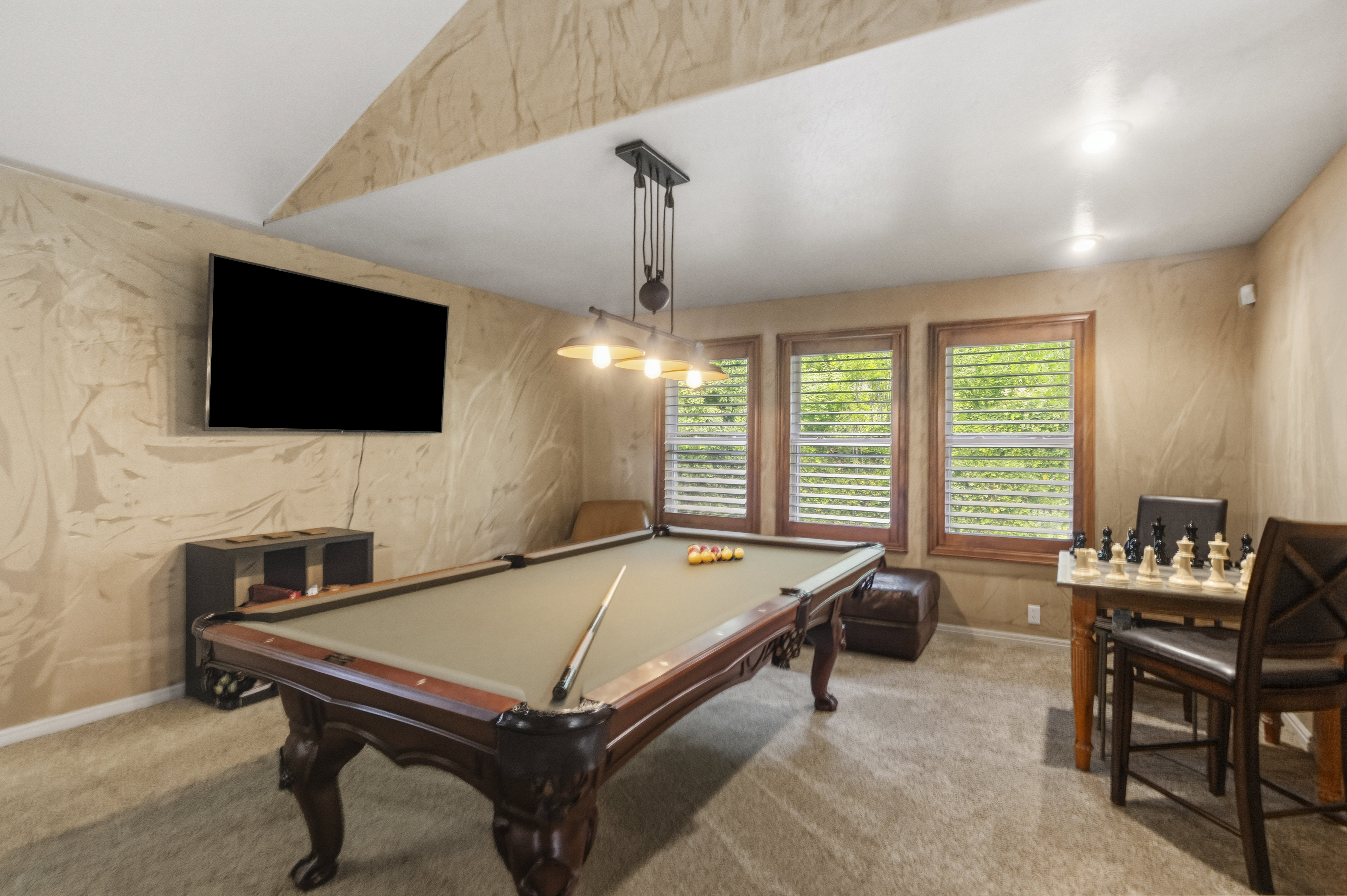 Recreation room featuring a billiards table with an overhead industrial-style light fixture, textured wall finishes, and three windows with louvered blinds