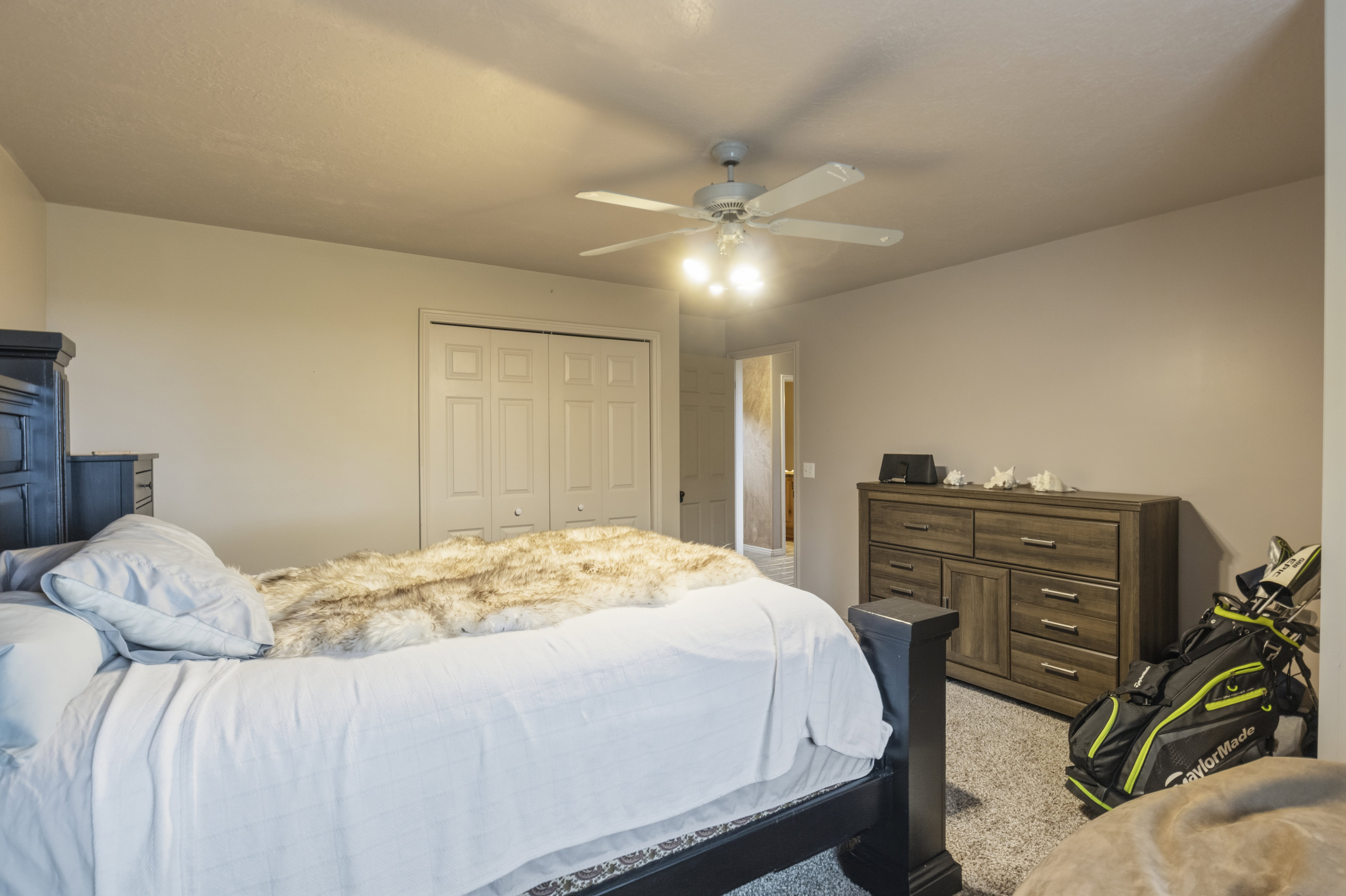 Carpeted bedroom featuring a ceiling fan with integrated lighting, dual bifold closet doors, and neutral wall tones