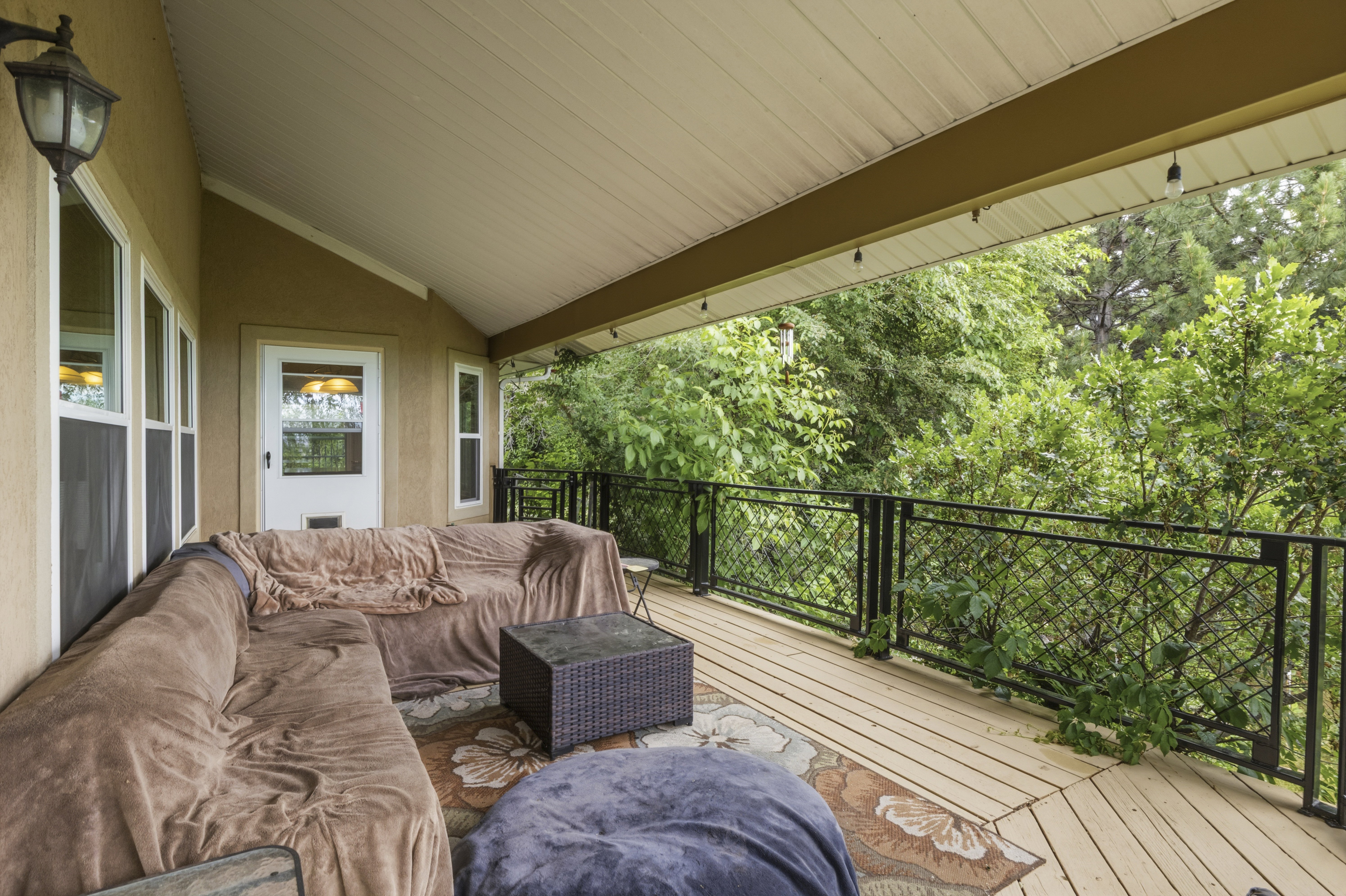 Covered outdoor deck featuring natural wood flooring and a black metal railing
