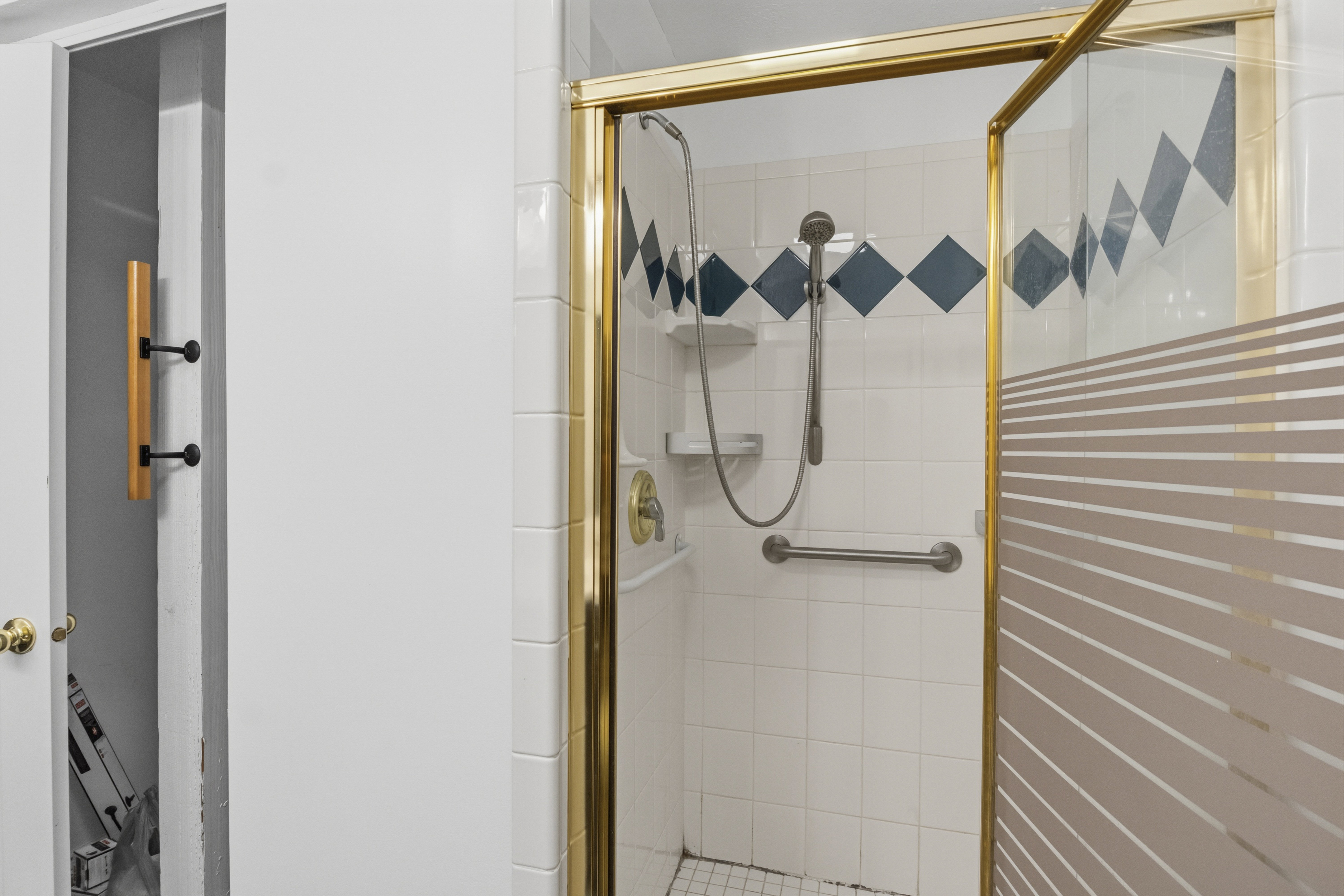 Shower stall with a gold-tone frame, white tiled walls, and decorative blue diamond accents