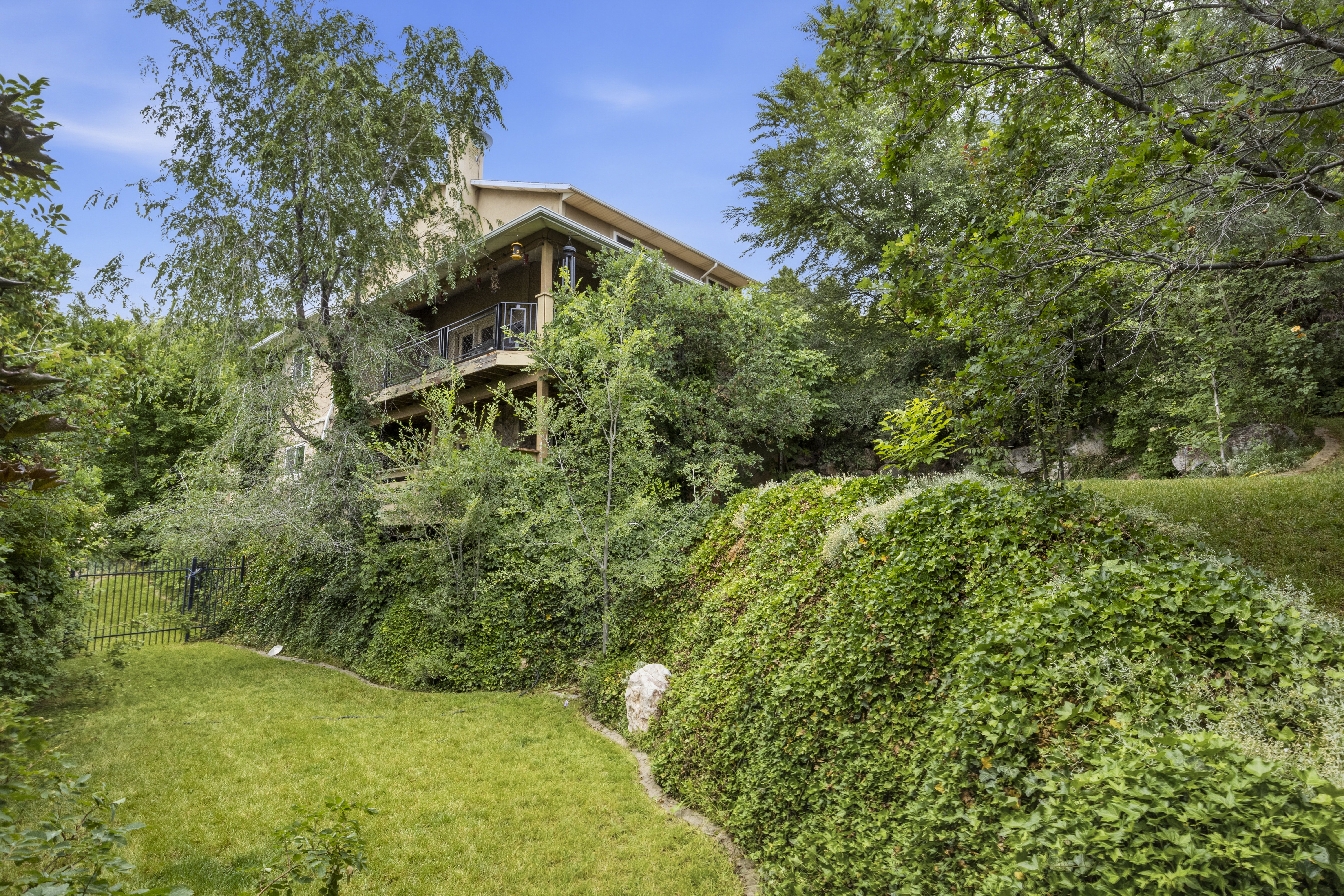 Tiered property featuring extensive greenery, a multi-level deck, and a private rear yard with a black metal fence