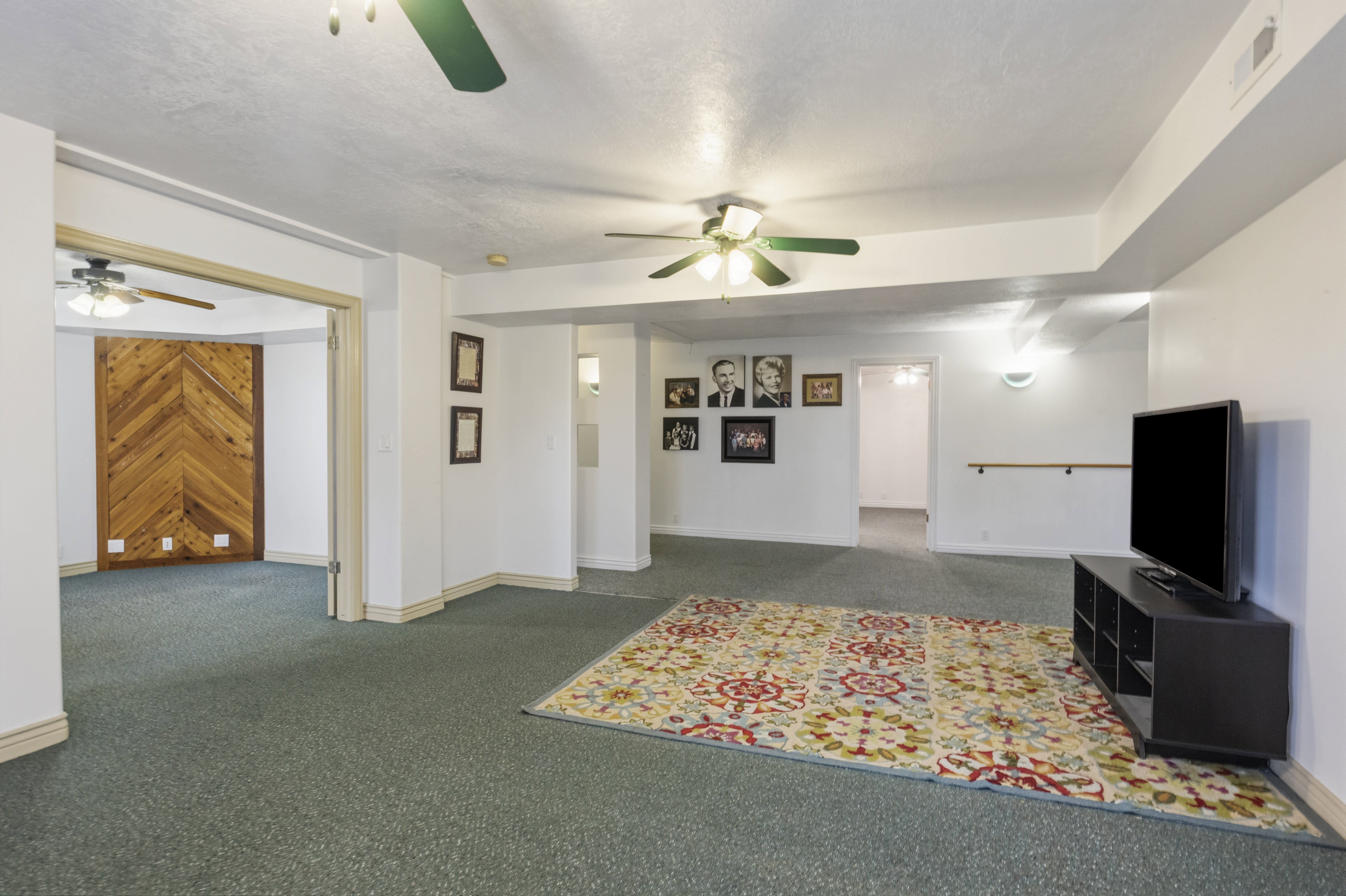 Spacious carpeted room featuring multiple ceiling fans, recessed lighting, and a prominent wood-finish accent wall with a chevron pattern