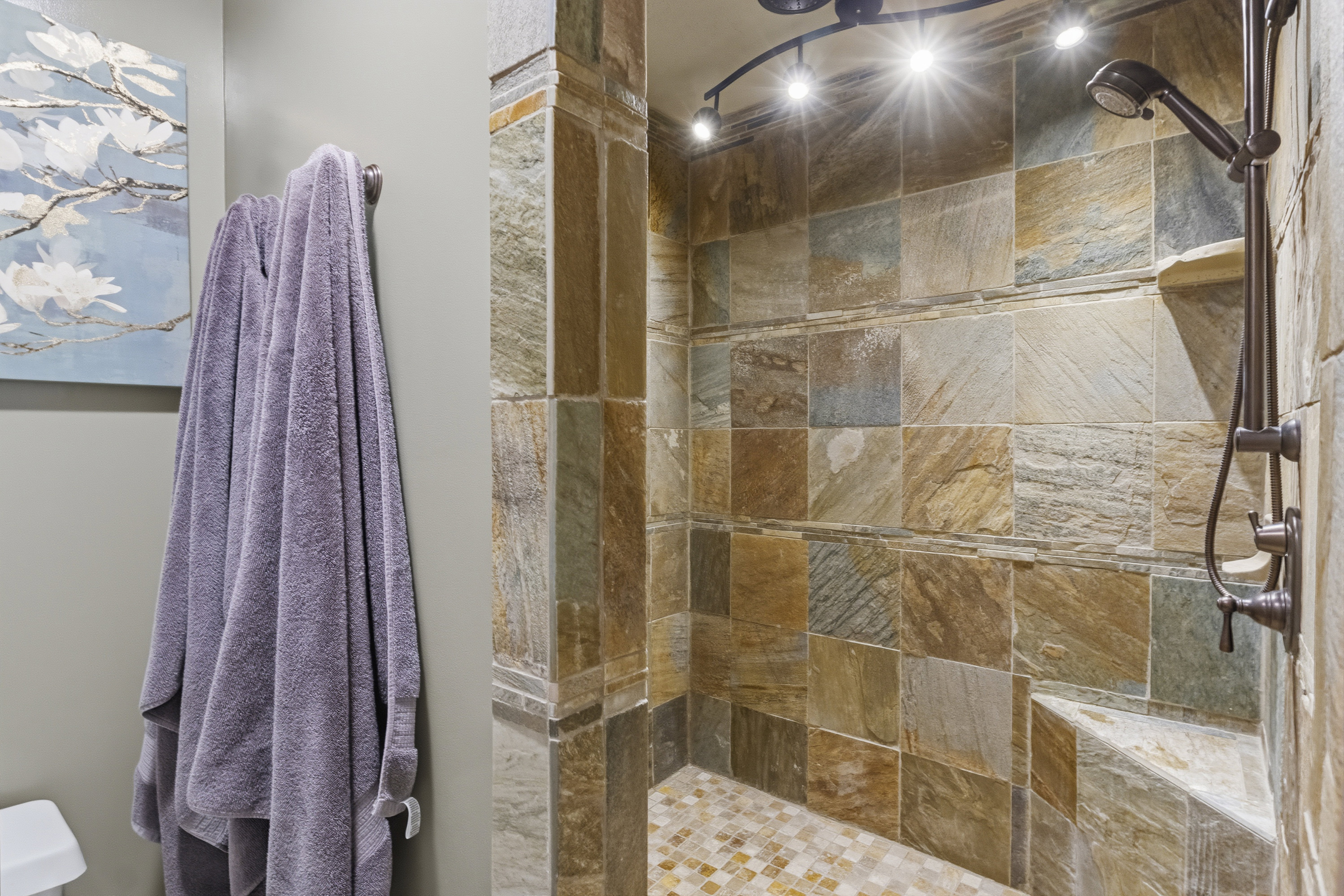 Tiled shower stall featuring a built-in bench, track lighting, and a handheld shower fixture