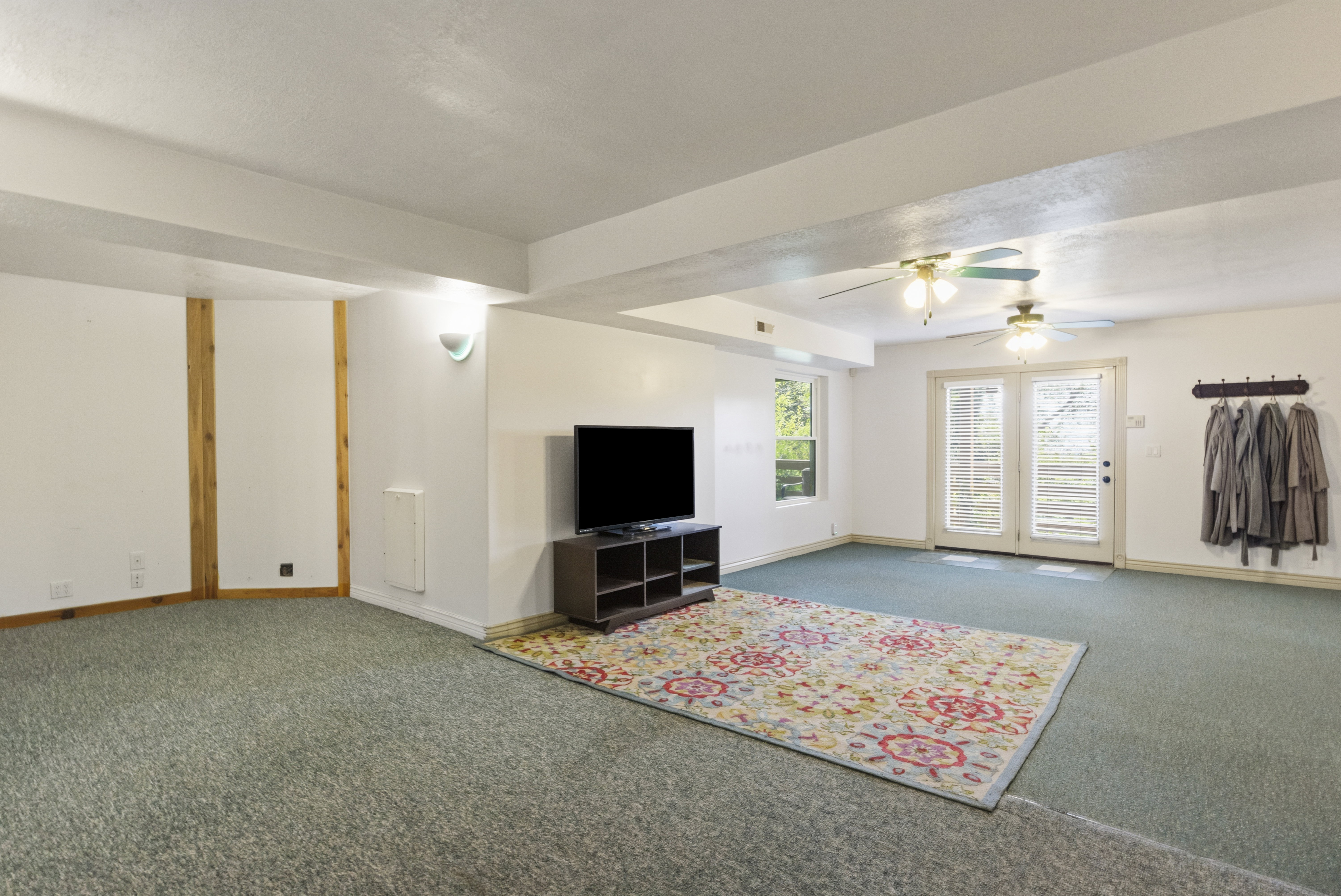 Spacious room featuring light green carpet, white walls, and exposed wood beam accents