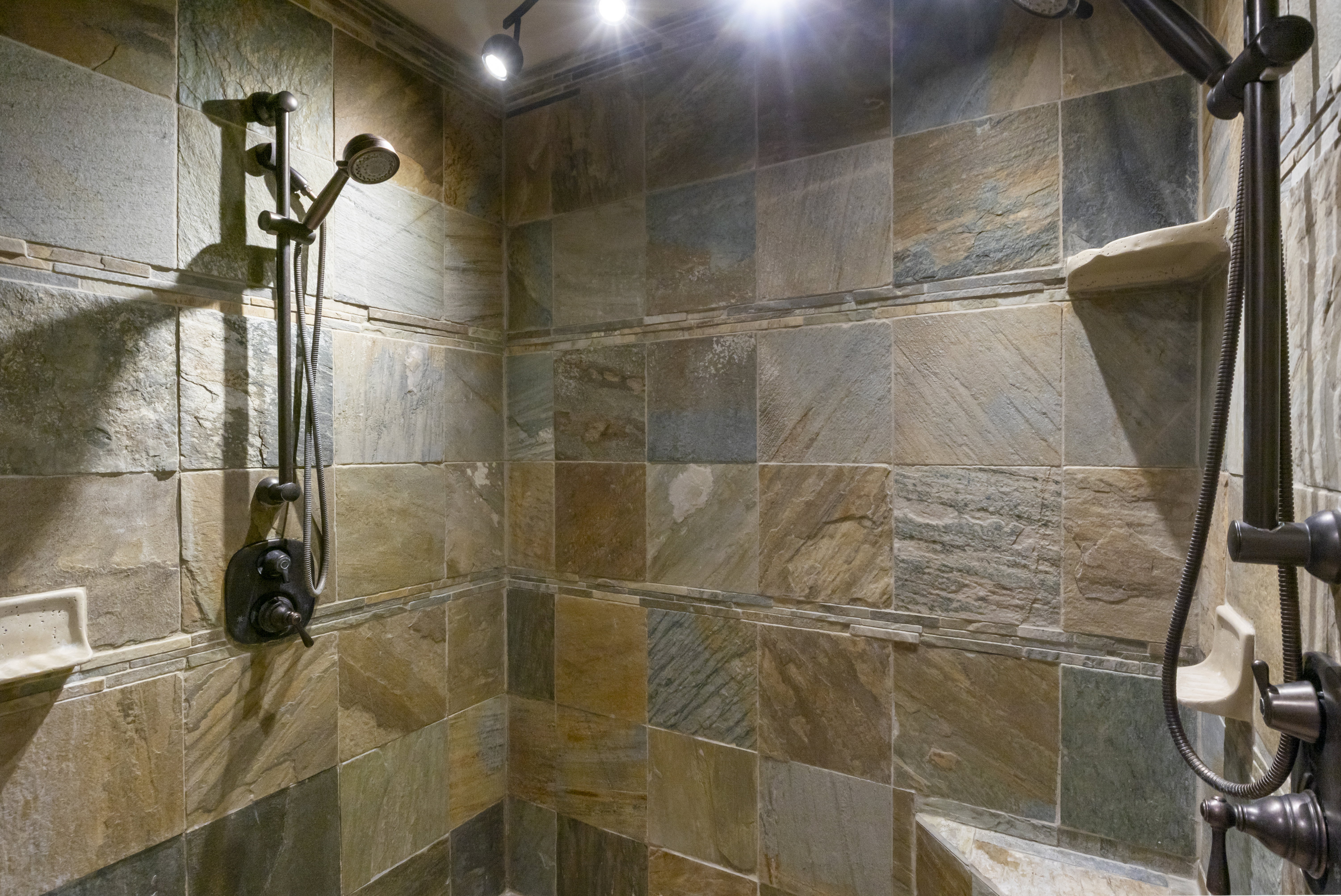 Shower enclosure featuring multi-toned slate tile walls and a built-in bench