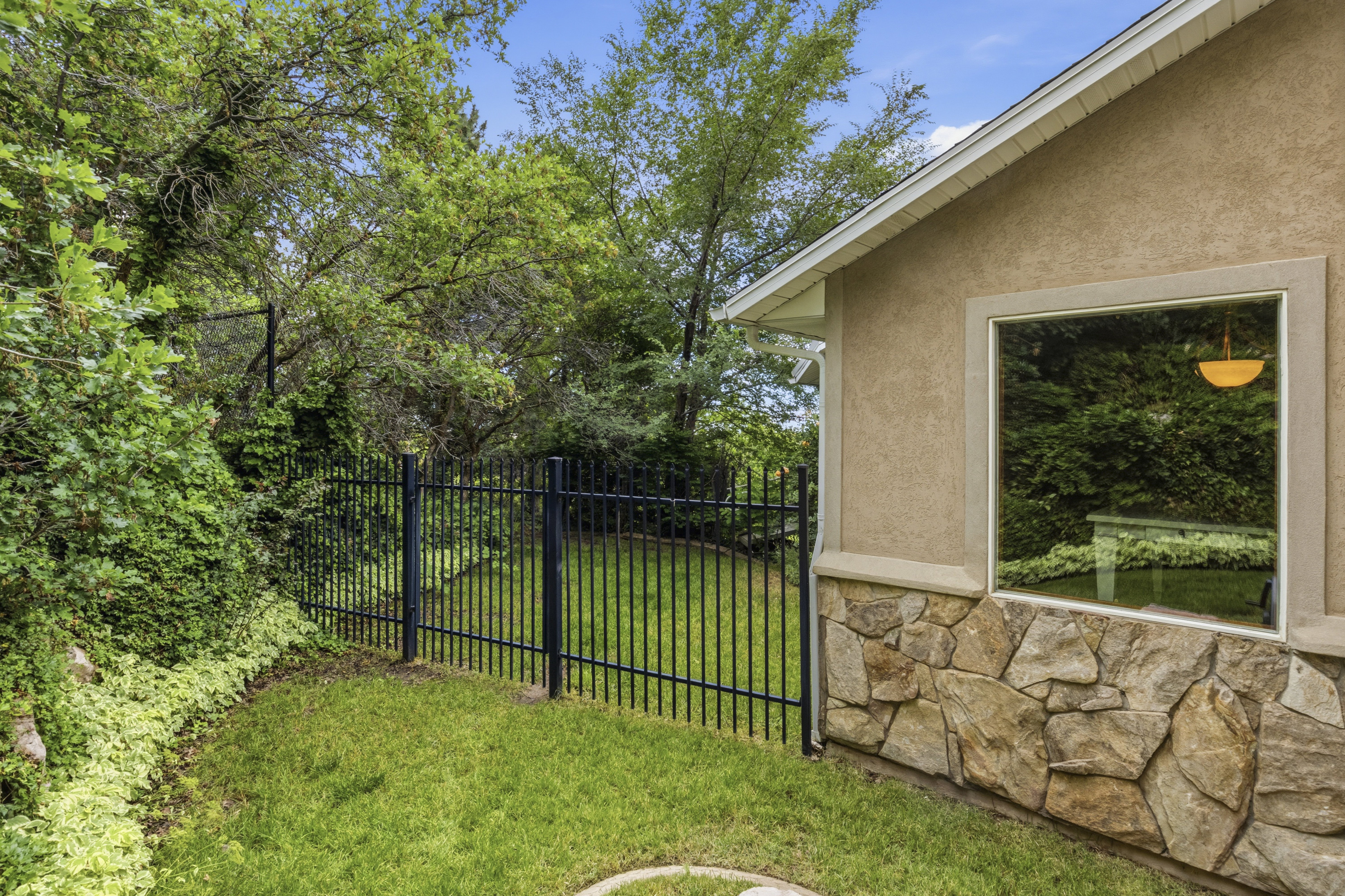 Side exterior featuring a stucco finish, stone veneer detailing, a large picture window, and a black wrought-iron fence