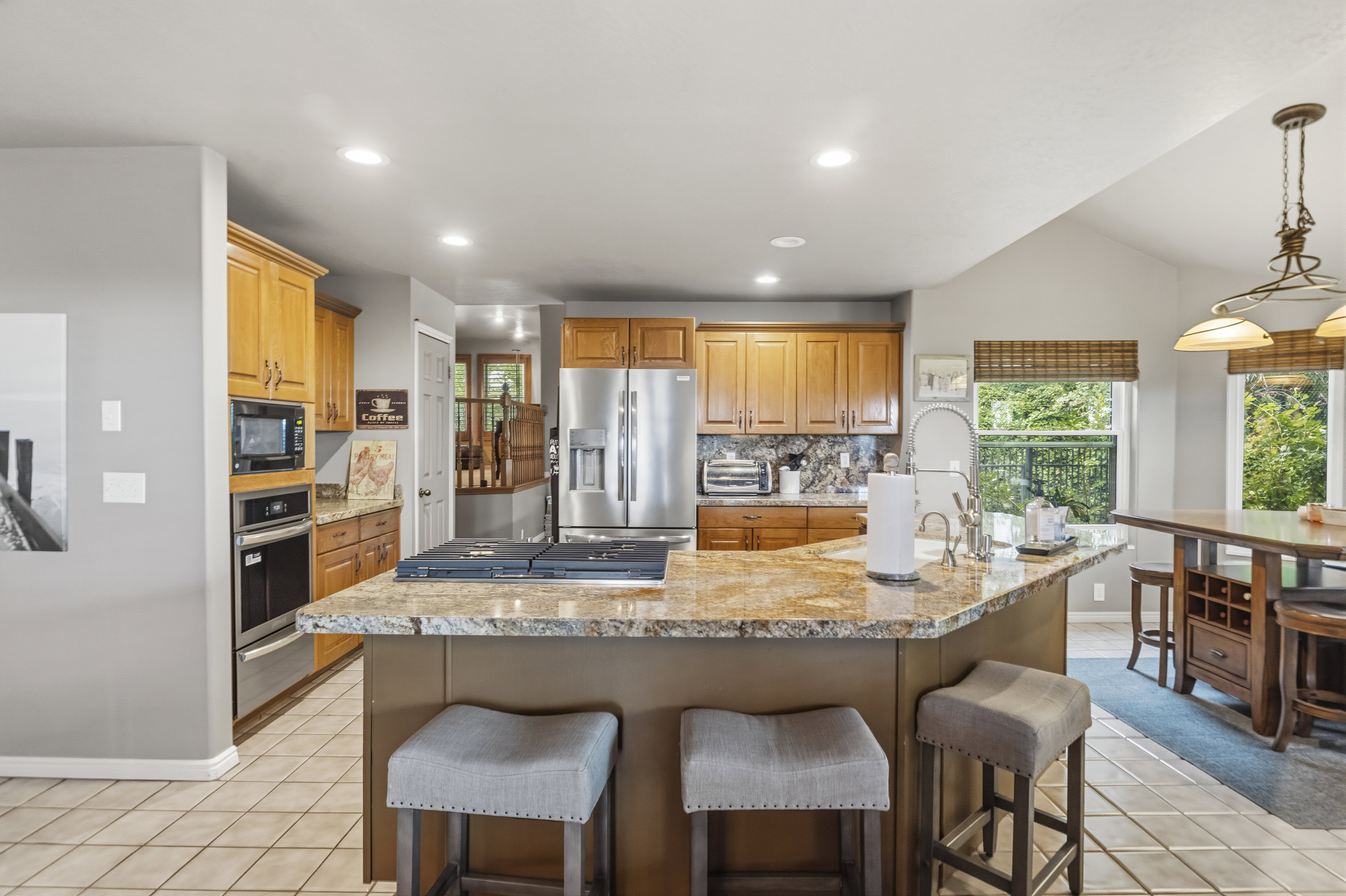 Expansive kitchen featuring a large island with a cooktop, granite countertops, wood cabinetry, stainless steel appliances, and tile flooring