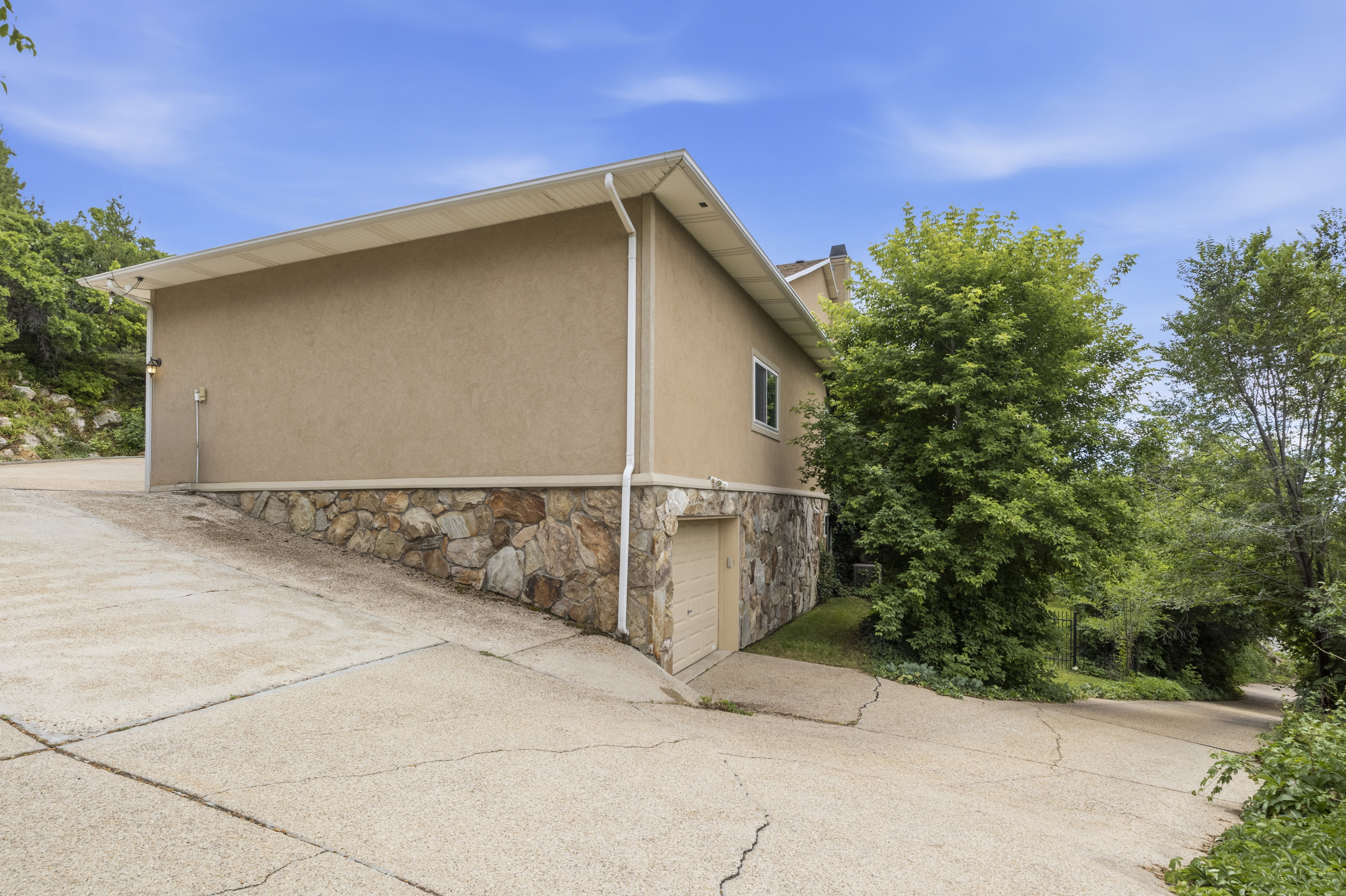 Exterior featuring stucco siding, a stone-clad foundation, and a lower-level garage door