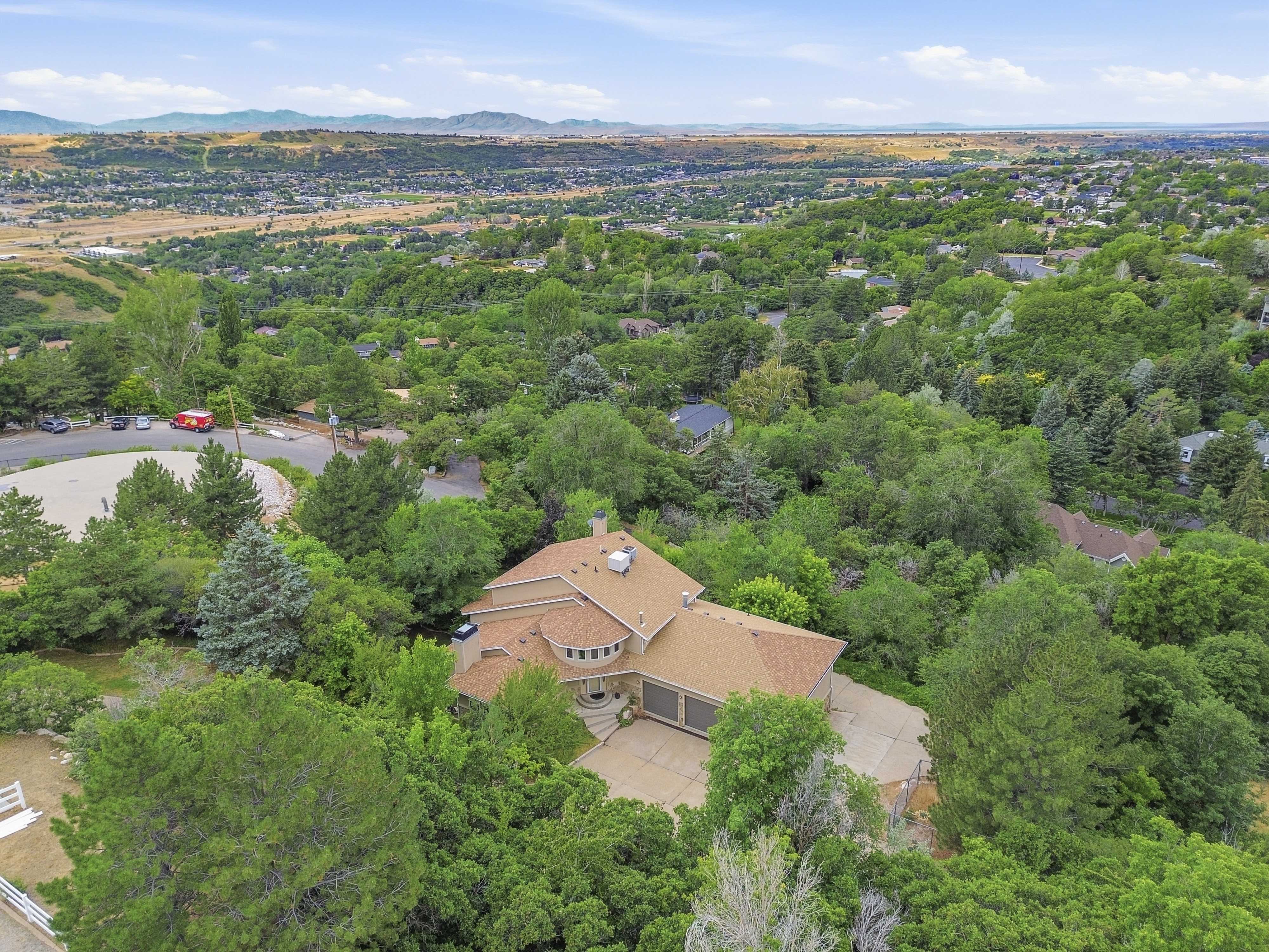 Expansive residential property featuring a large home, mature trees, a multi-car driveway, and a distant mountain backdrop