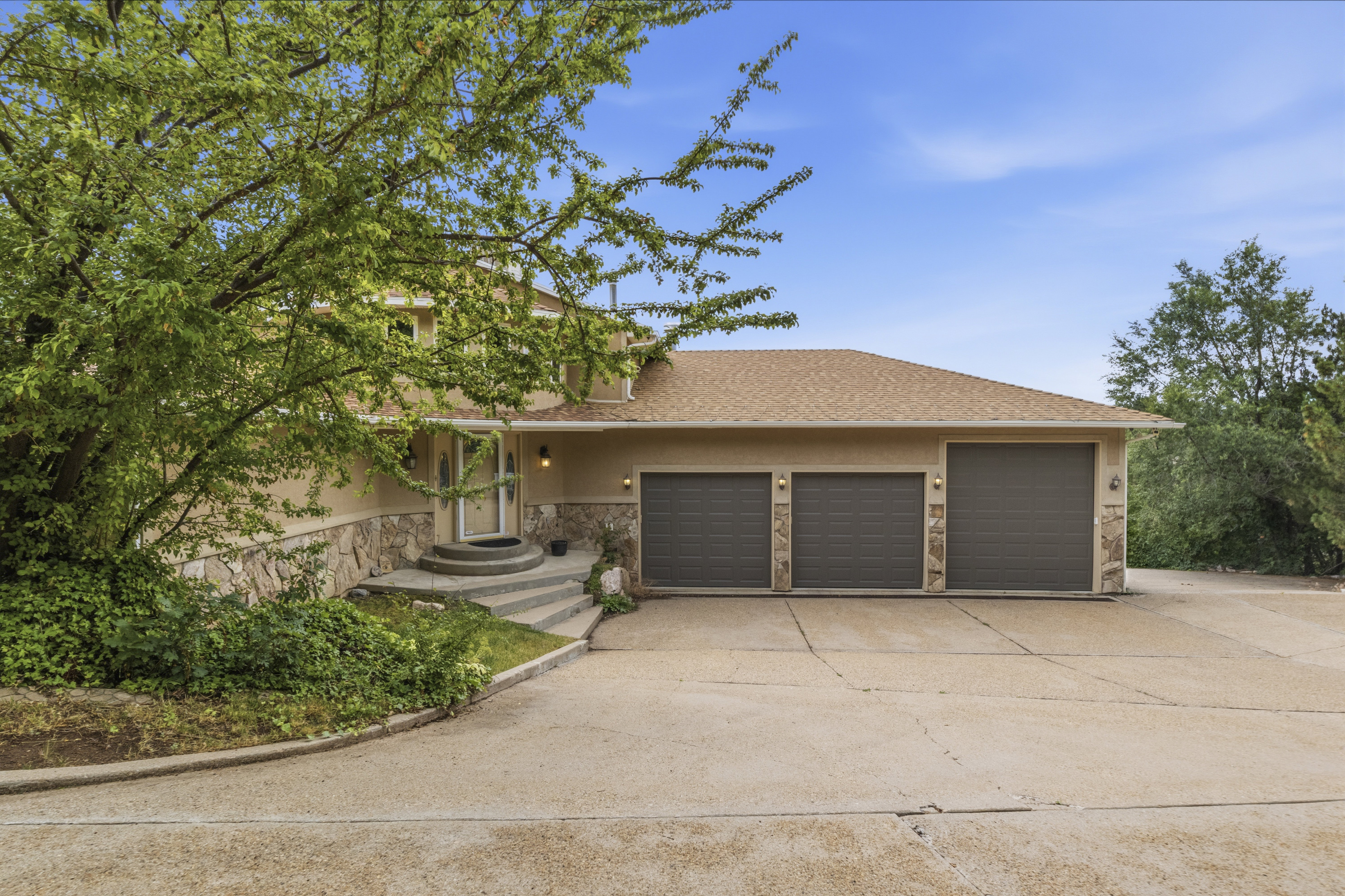Stucco exterior featuring stone accents, a three-car garage, concrete driveway, and a tiered concrete walkway to the front entry
