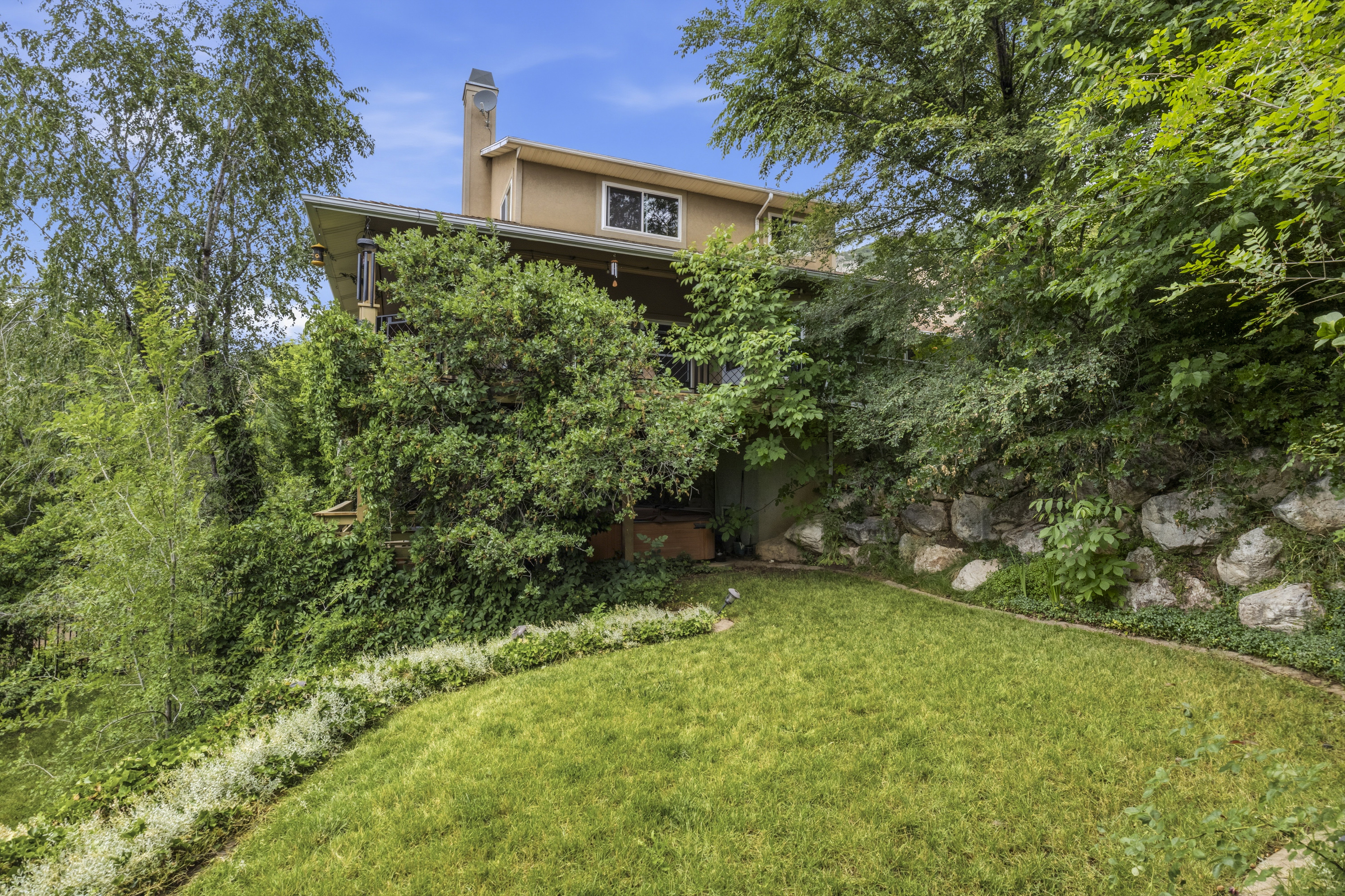 Terraced property featuring a manicured lawn, stone retaining wall, and a covered balcony