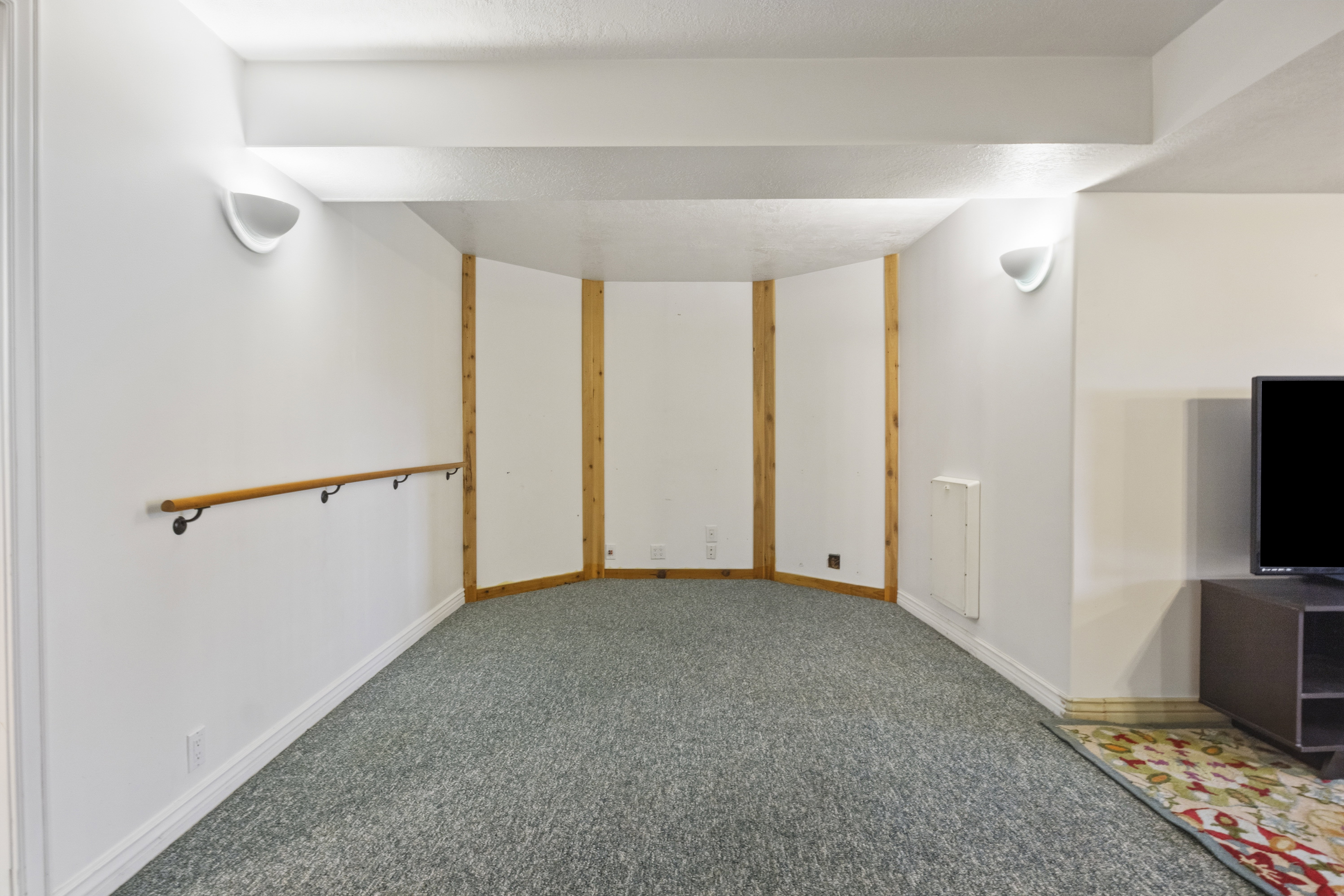 Recreational space featuring wall-mounted wooden barre, sconce lighting, and a neutral carpeted floor
