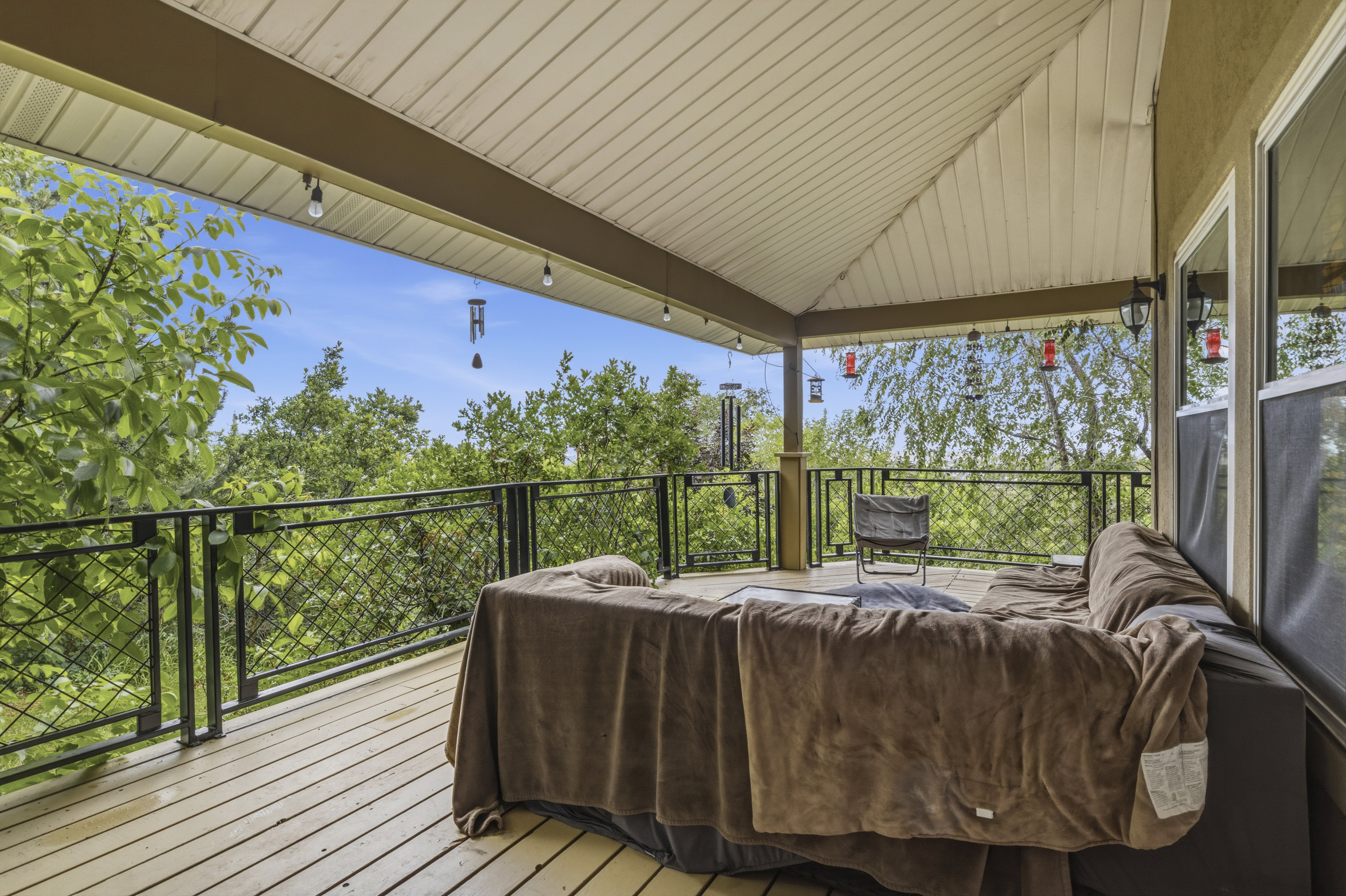 Covered outdoor deck with light wood-finish flooring, featuring a black metal railing