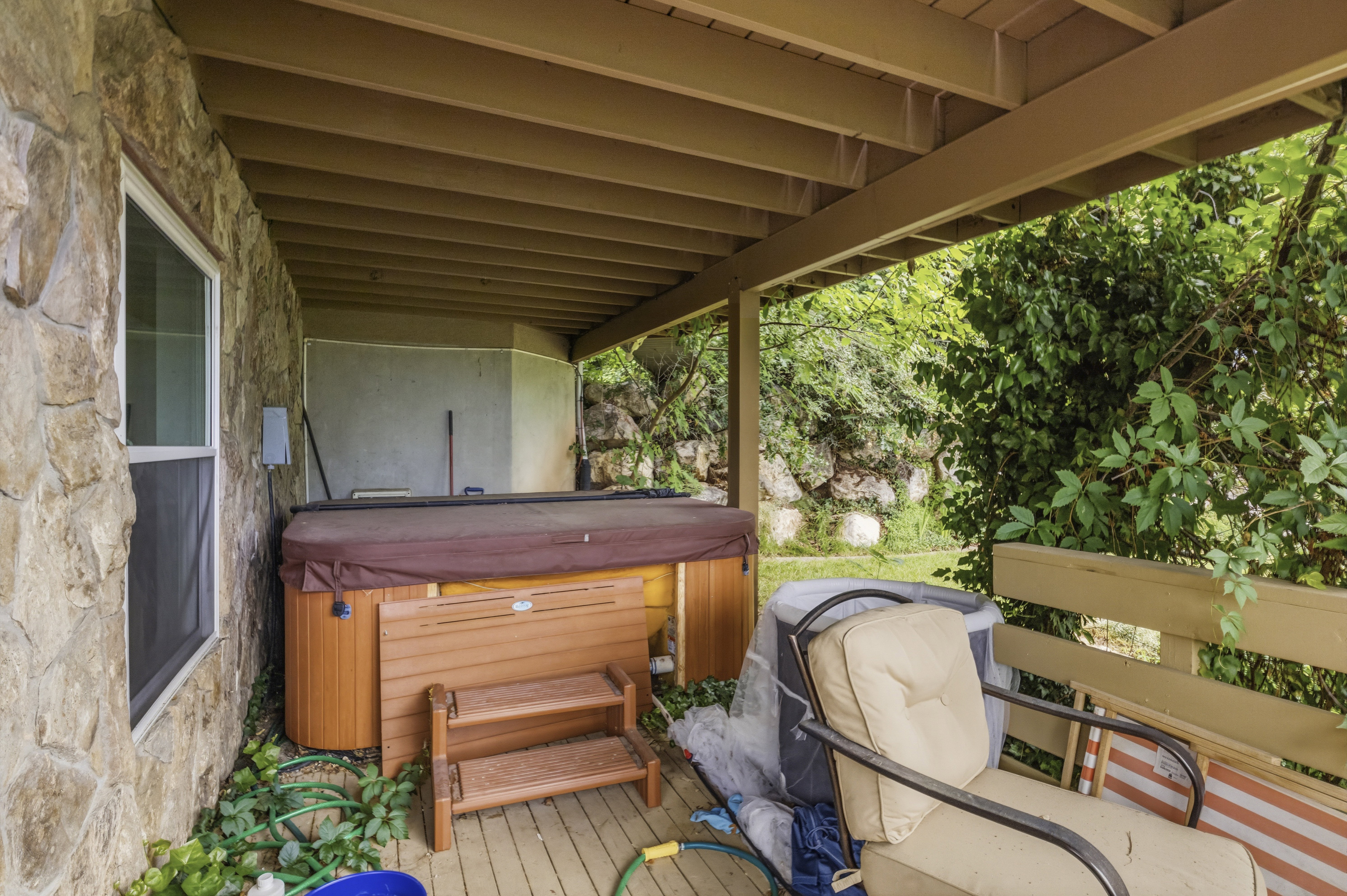 Covered outdoor patio featuring a hot tub, wood-finish decking, and a stone exterior wall