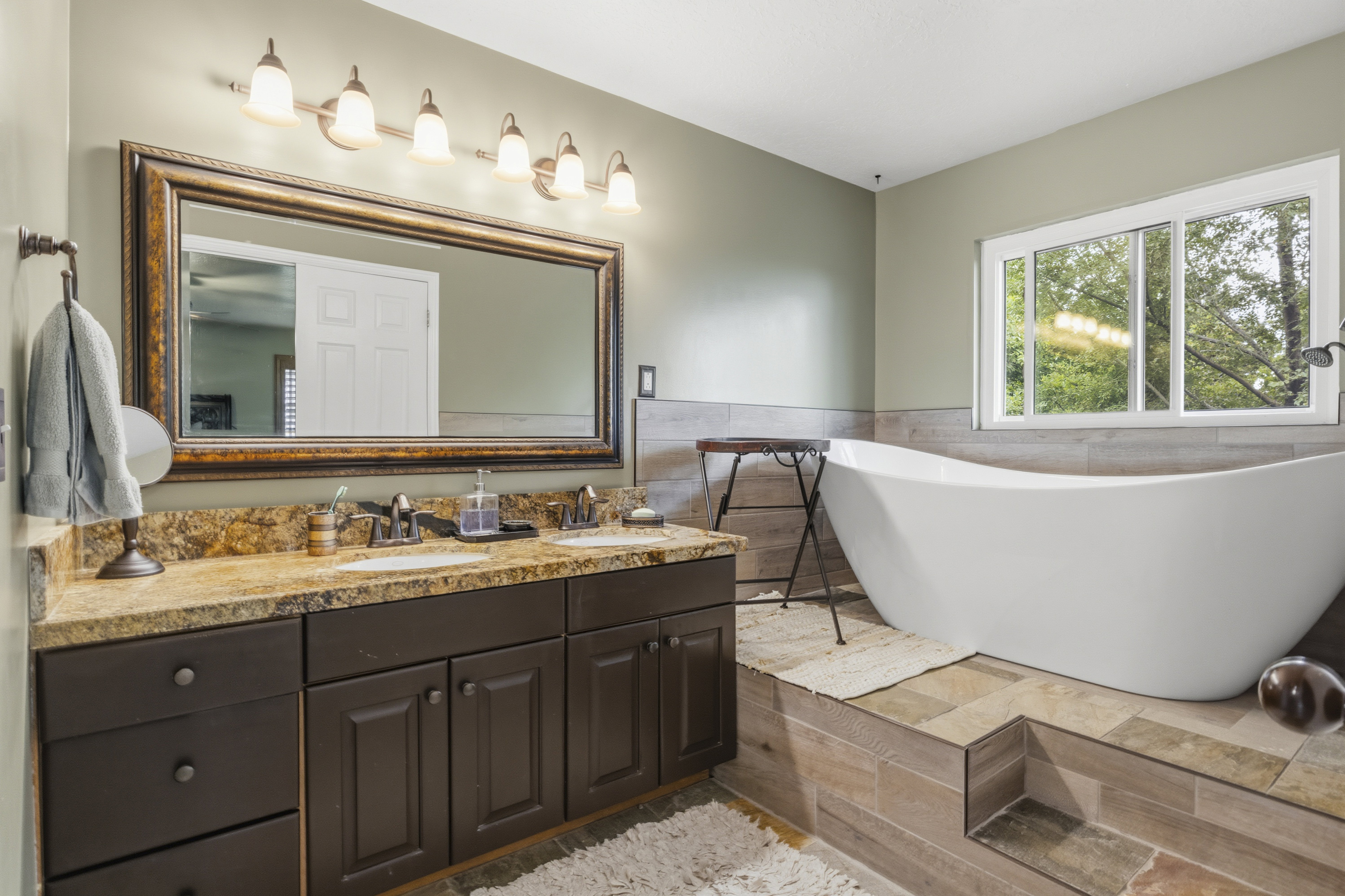 Bathroom featuring a freestanding soaking tub, dual vanity with undermount sinks, bronze hardware, a large framed mirror, and a multi-pane window