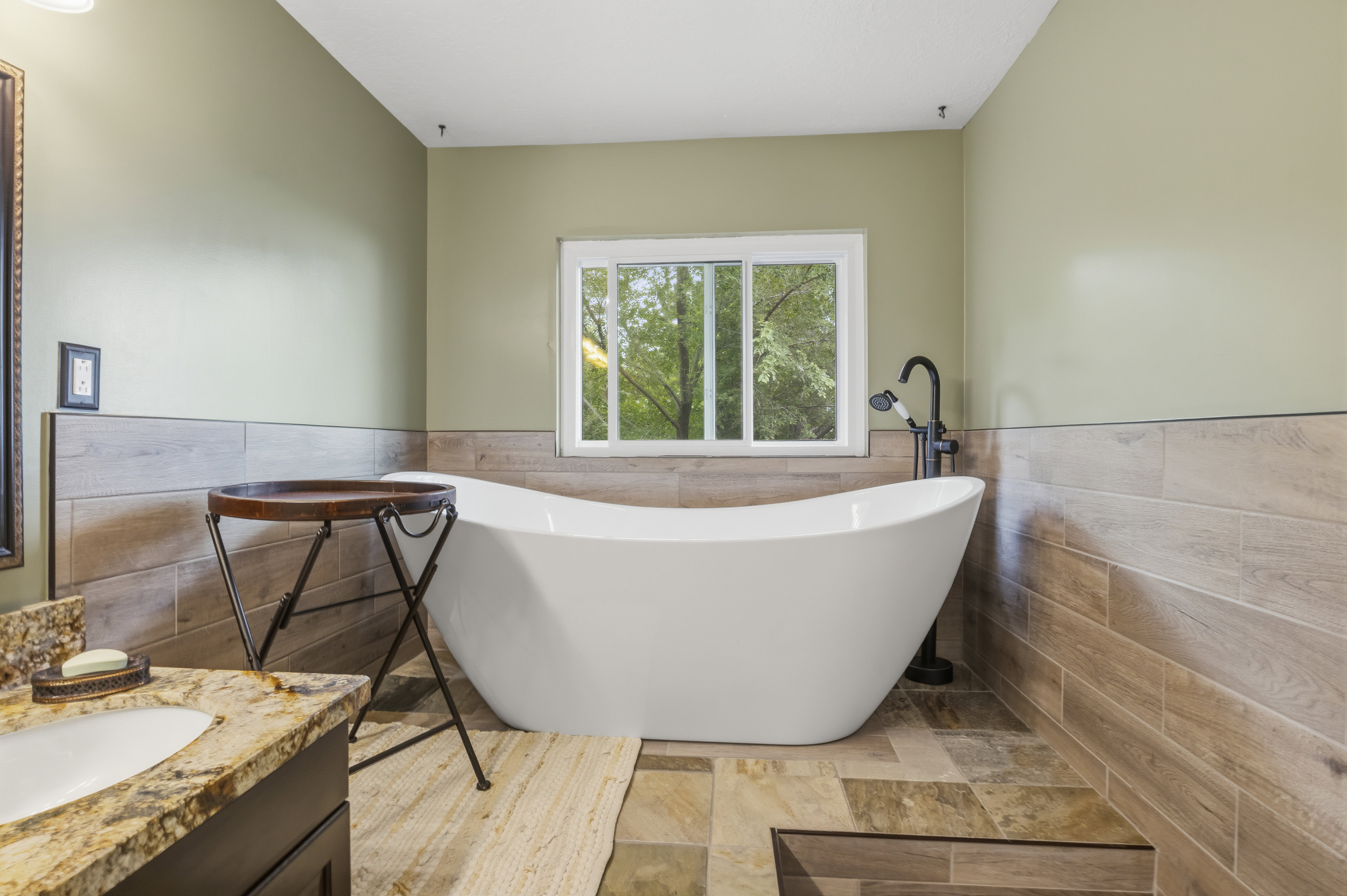 Freestanding soaking tub with a floor-mounted matte black faucet, set against a window
