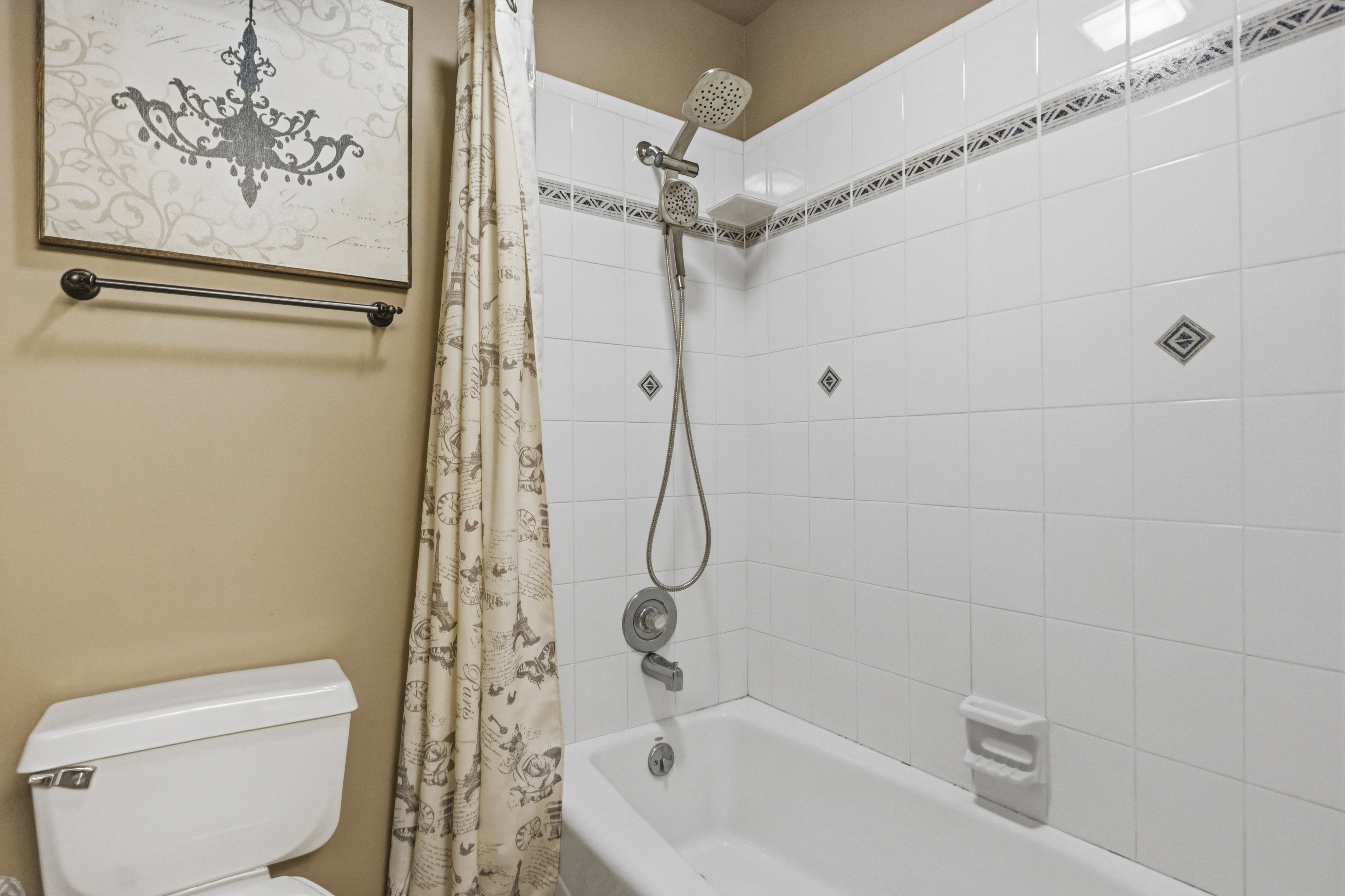Bathtub with white tile surround, decorative accent tiles, and a multi-function shower head