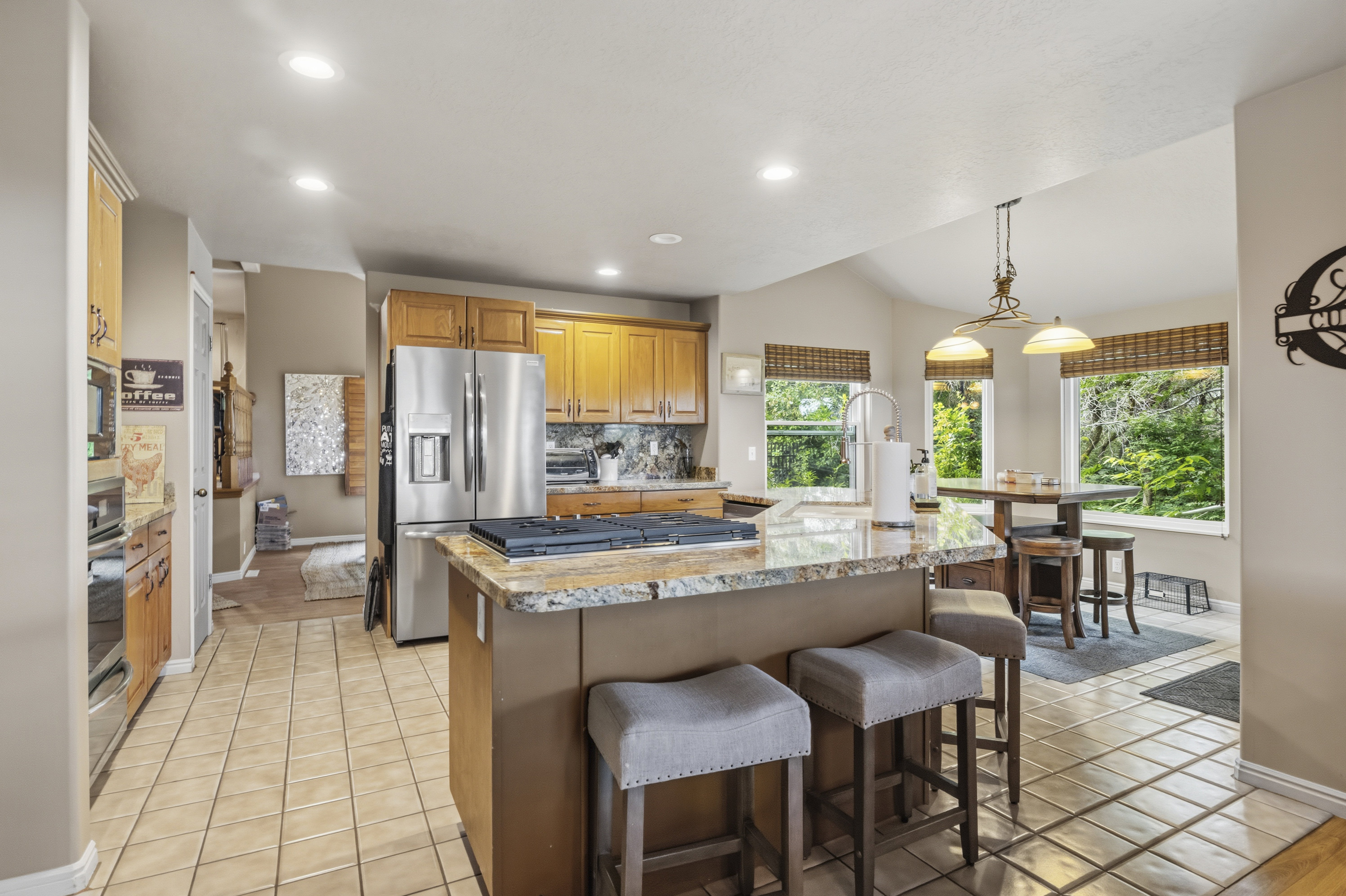 Kitchen featuring a central island with a built-in cooktop, light-toned wood cabinetry, stainless steel appliances, tile flooring, and multiple windows