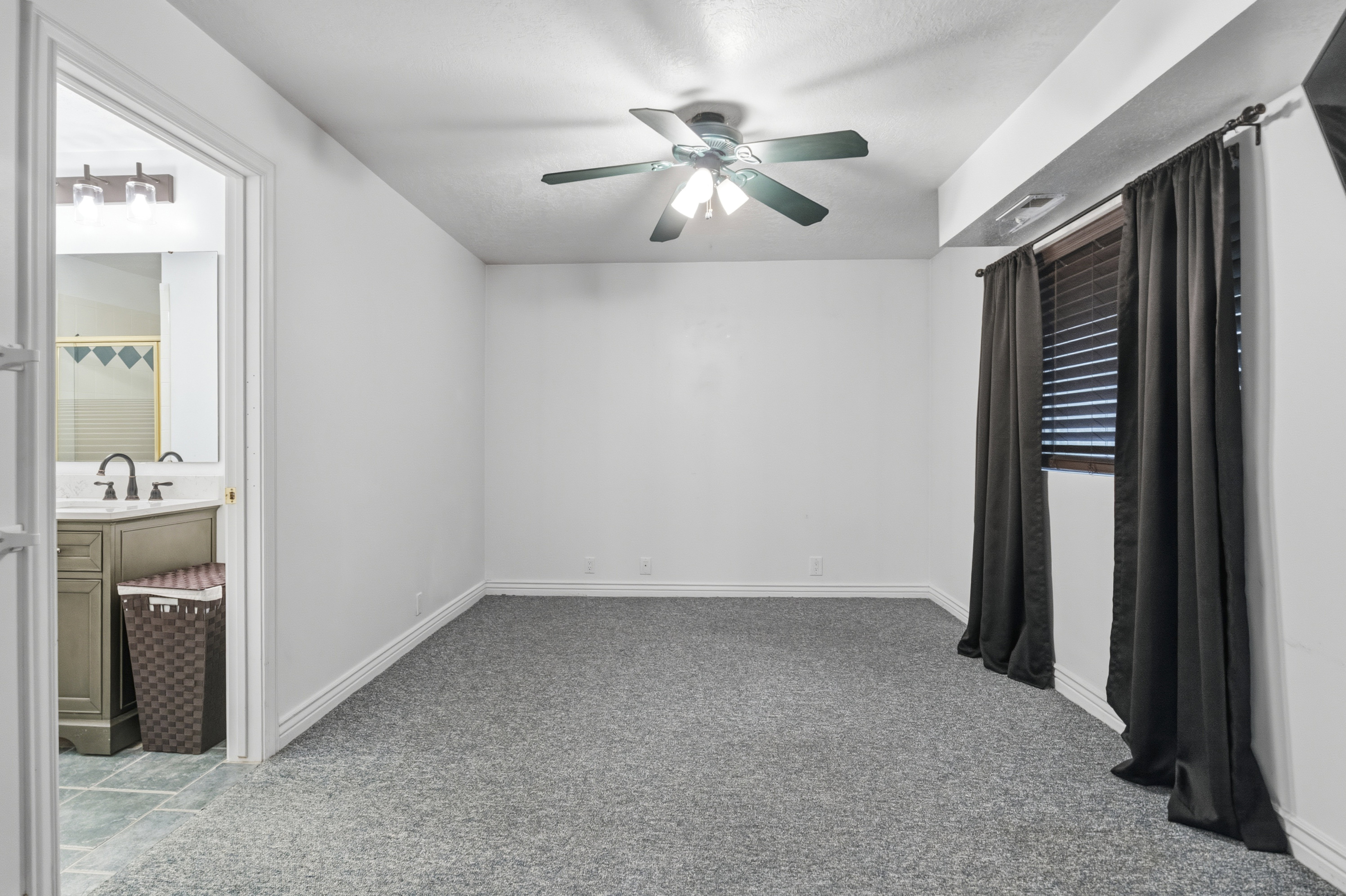 Spacious room with gray textured carpeting, white walls, and a ceiling fan with integrated lighting