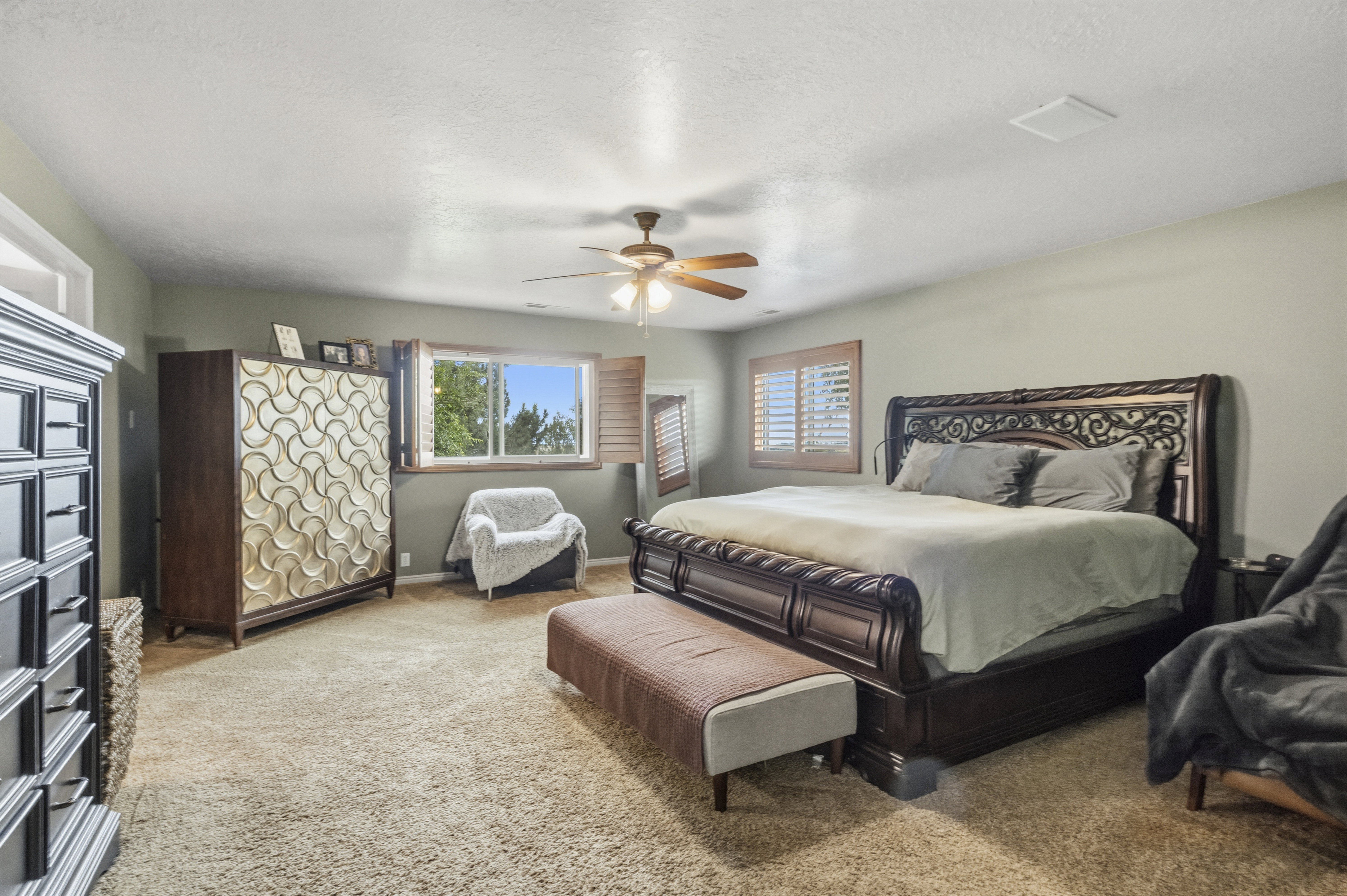 Carpeted bedroom featuring a ceiling fan, a window with plantation shutters, and a sloped ceiling