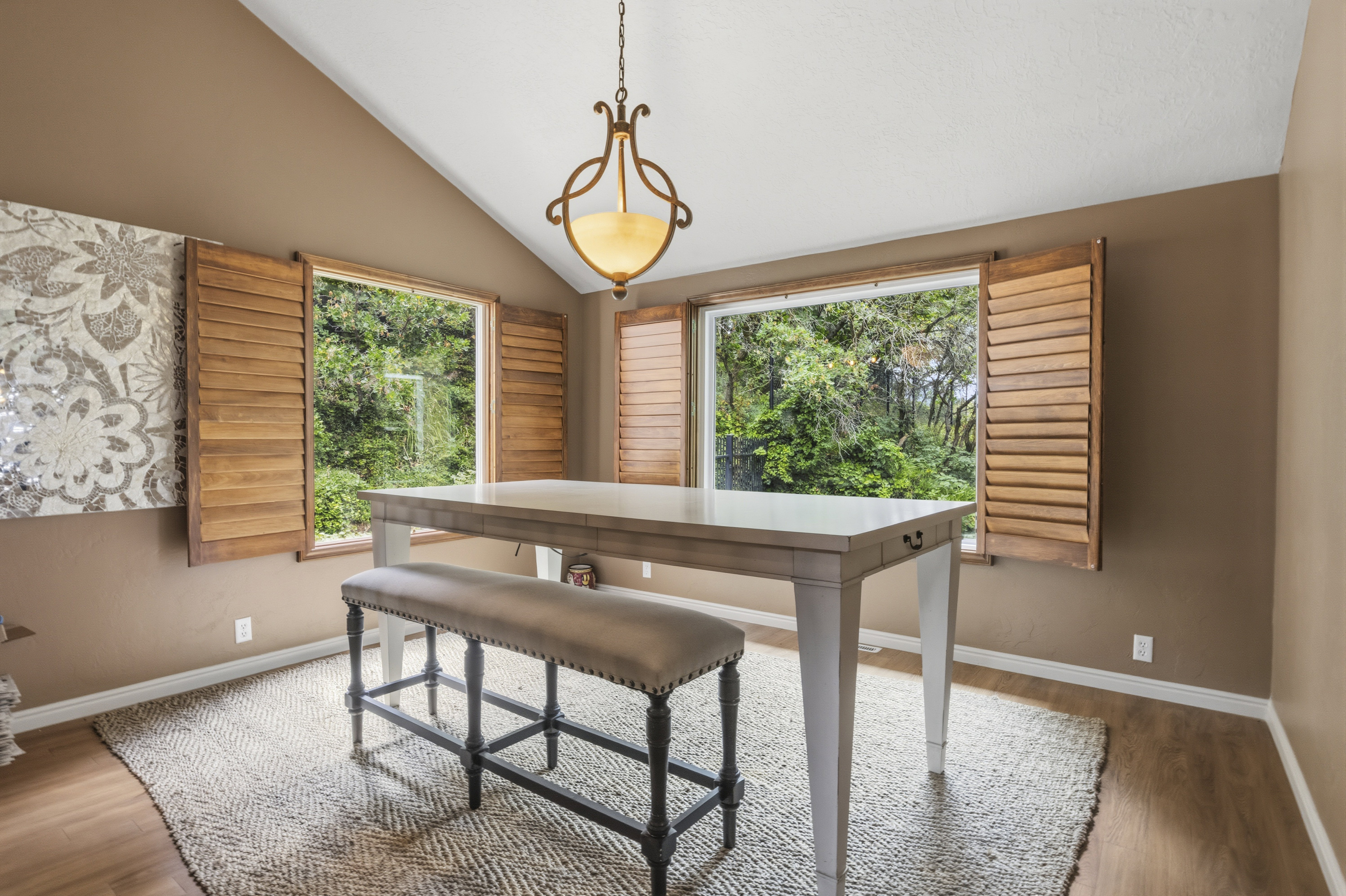 Room featuring vaulted ceiling, wood-finish flooring, and two windows with wood plantation shutters