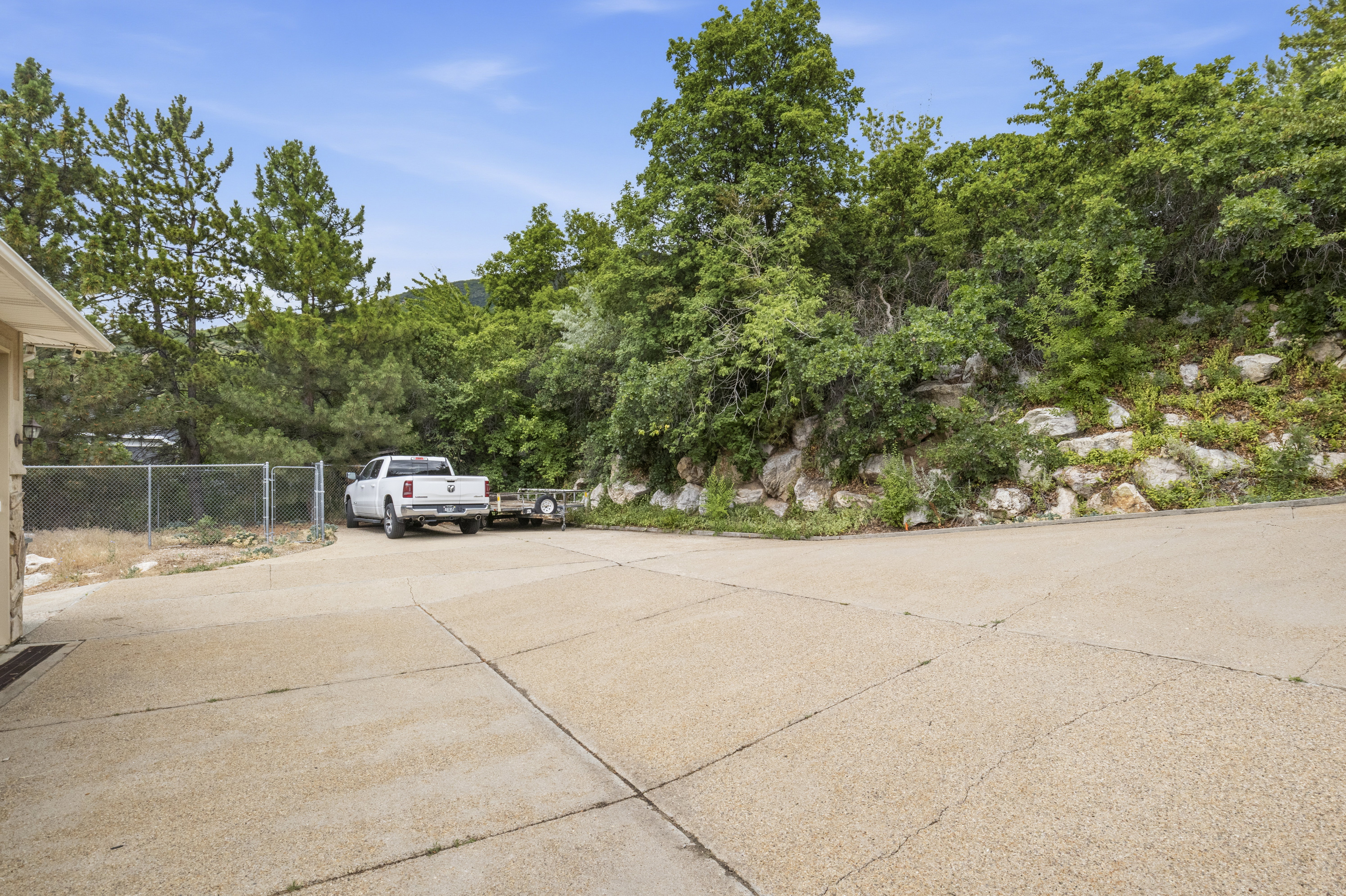 Expansive concrete driveway with a gravel aggregate finish, bordered by mature trees and natural rock landscaping