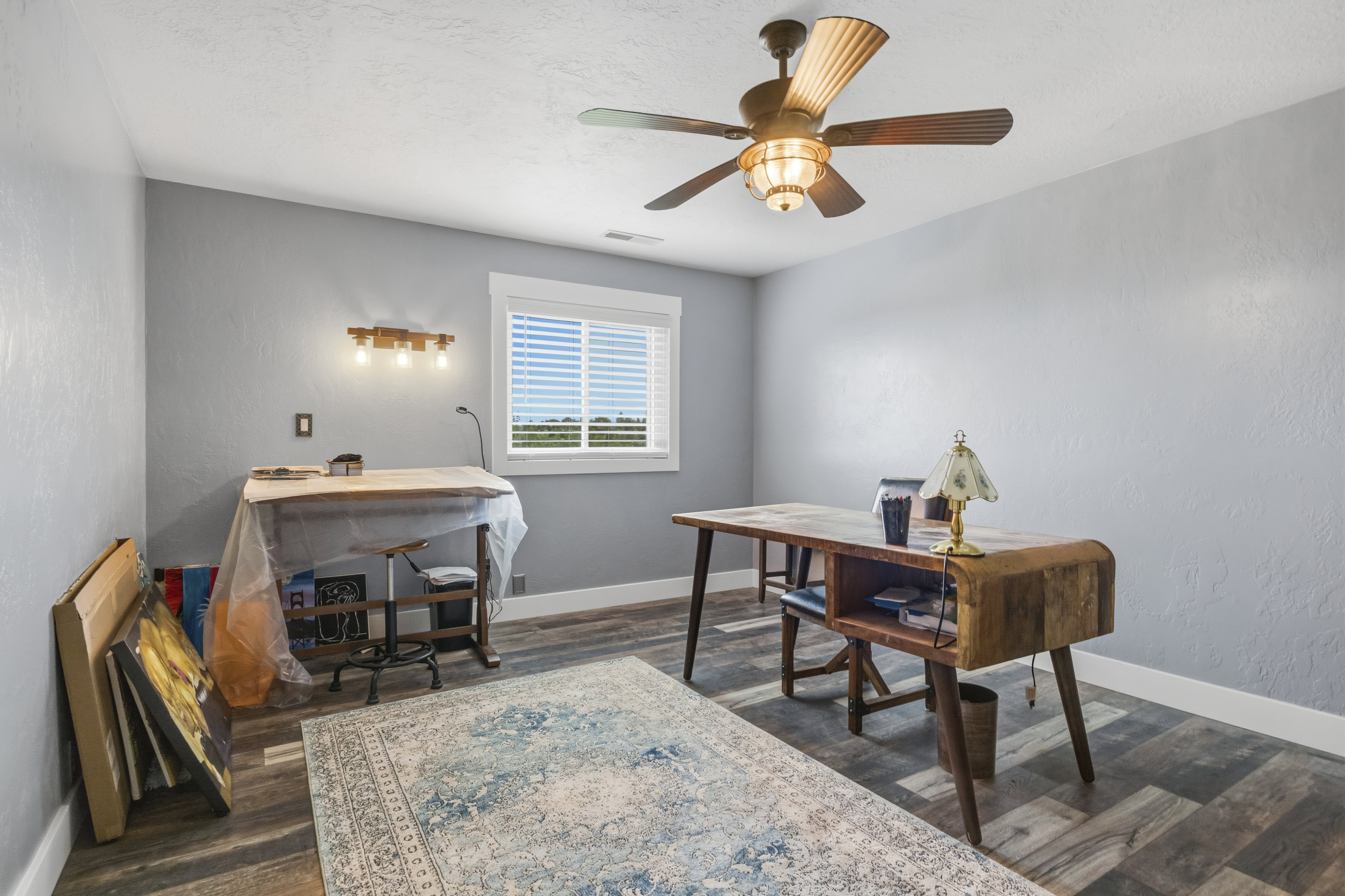 Bright interior space featuring wood-finish flooring, a ceiling fan with integrated lighting, and a window with blinds