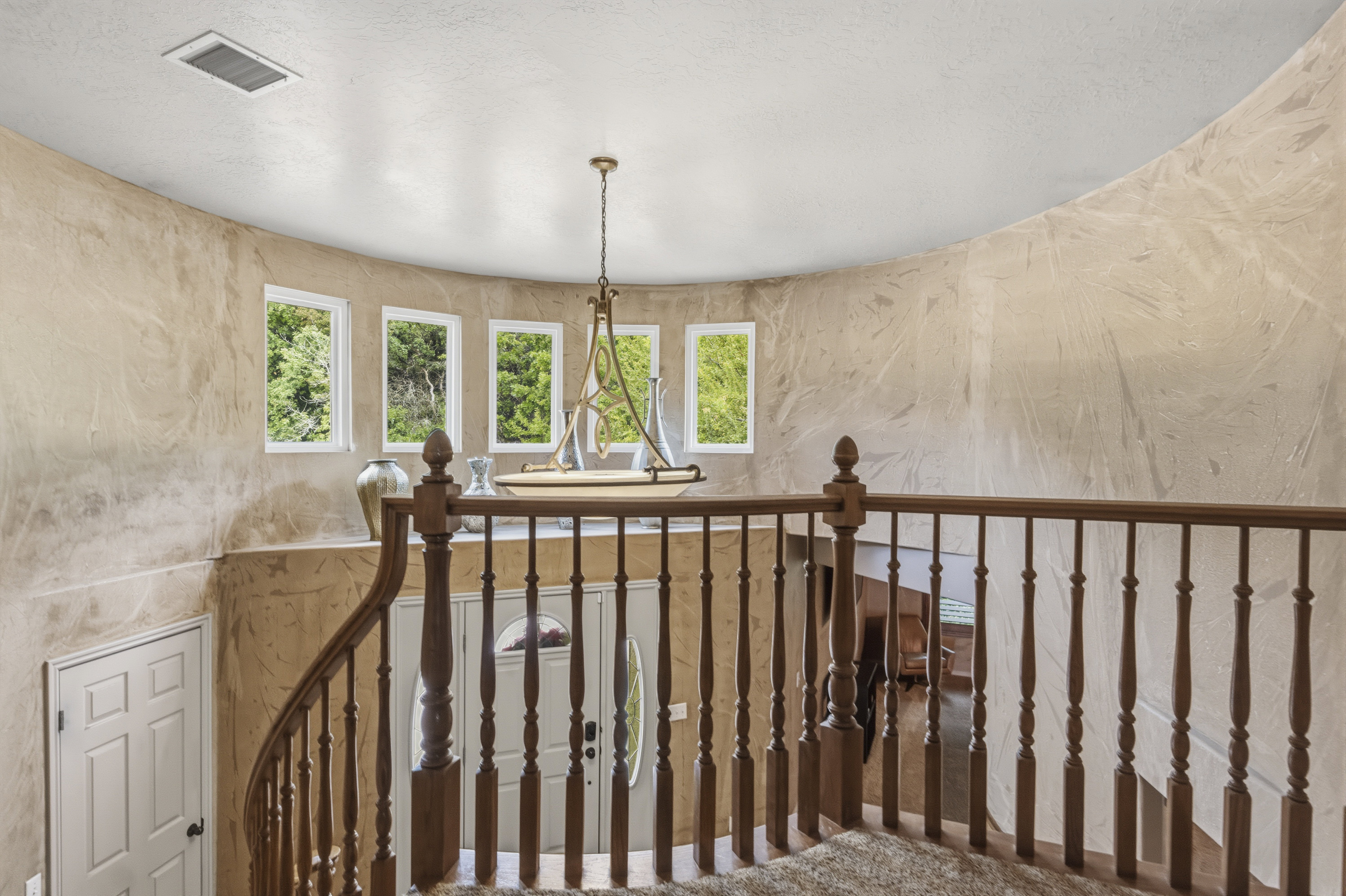 Curved stairwell with wood balusters and a decorative chandelier