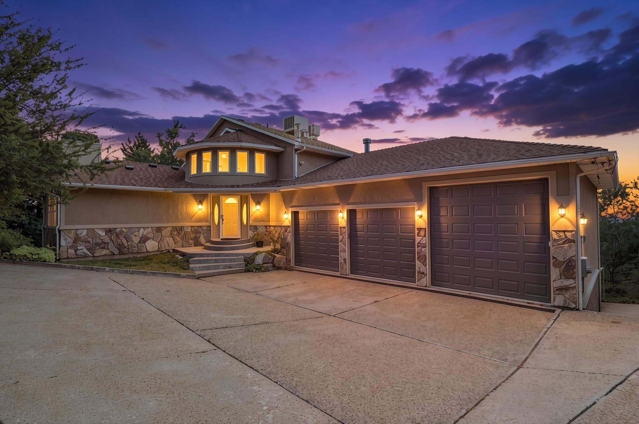 Exterior facade featuring a three-car garage, stone veneer accents, an elevated entry with steps, and a circular architectural element with multiple windows