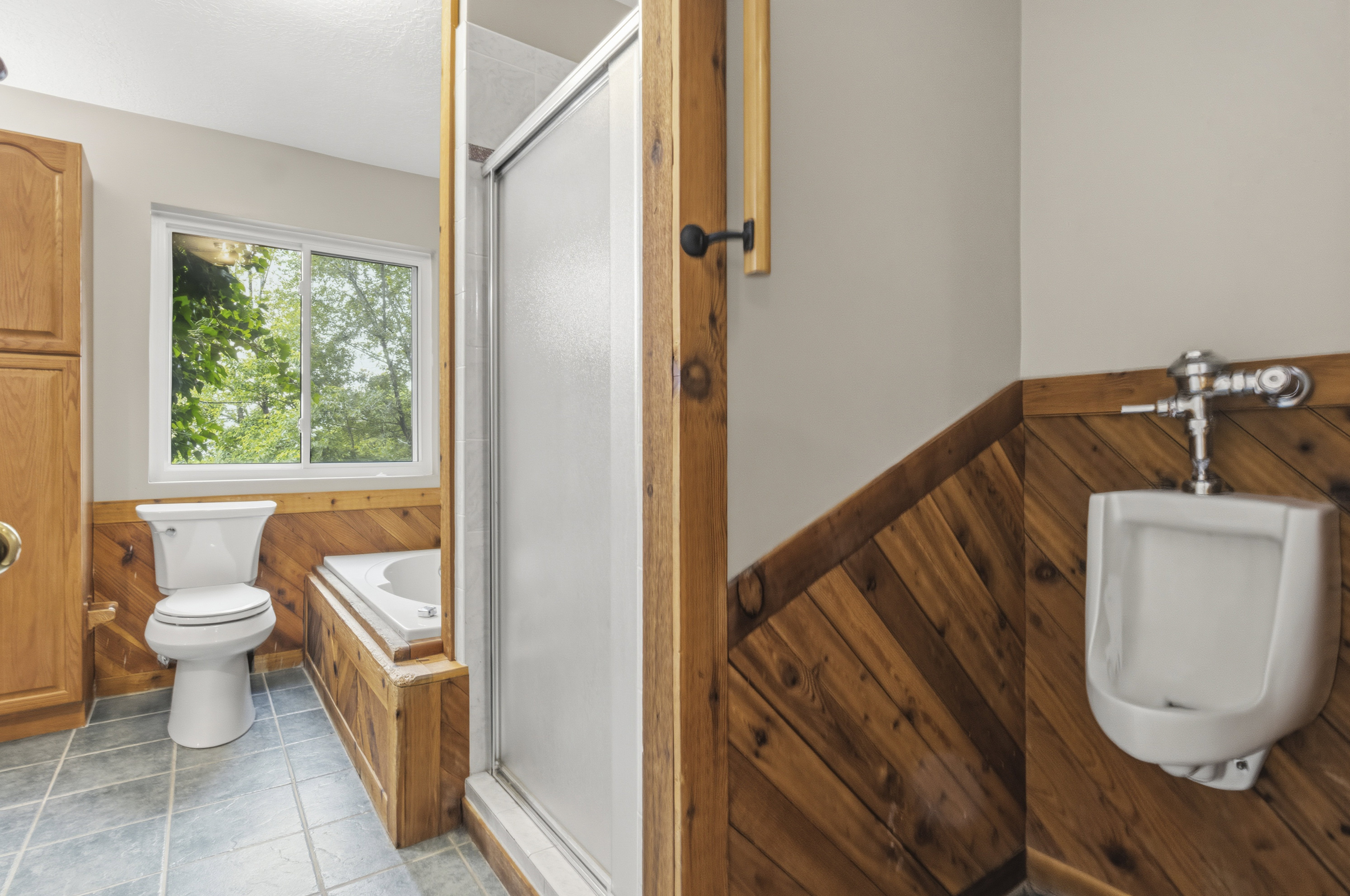 Bathroom featuring wood-paneled wainscoting, tiled flooring, a built-in tub, and a separate shower enclosure with a sliding door