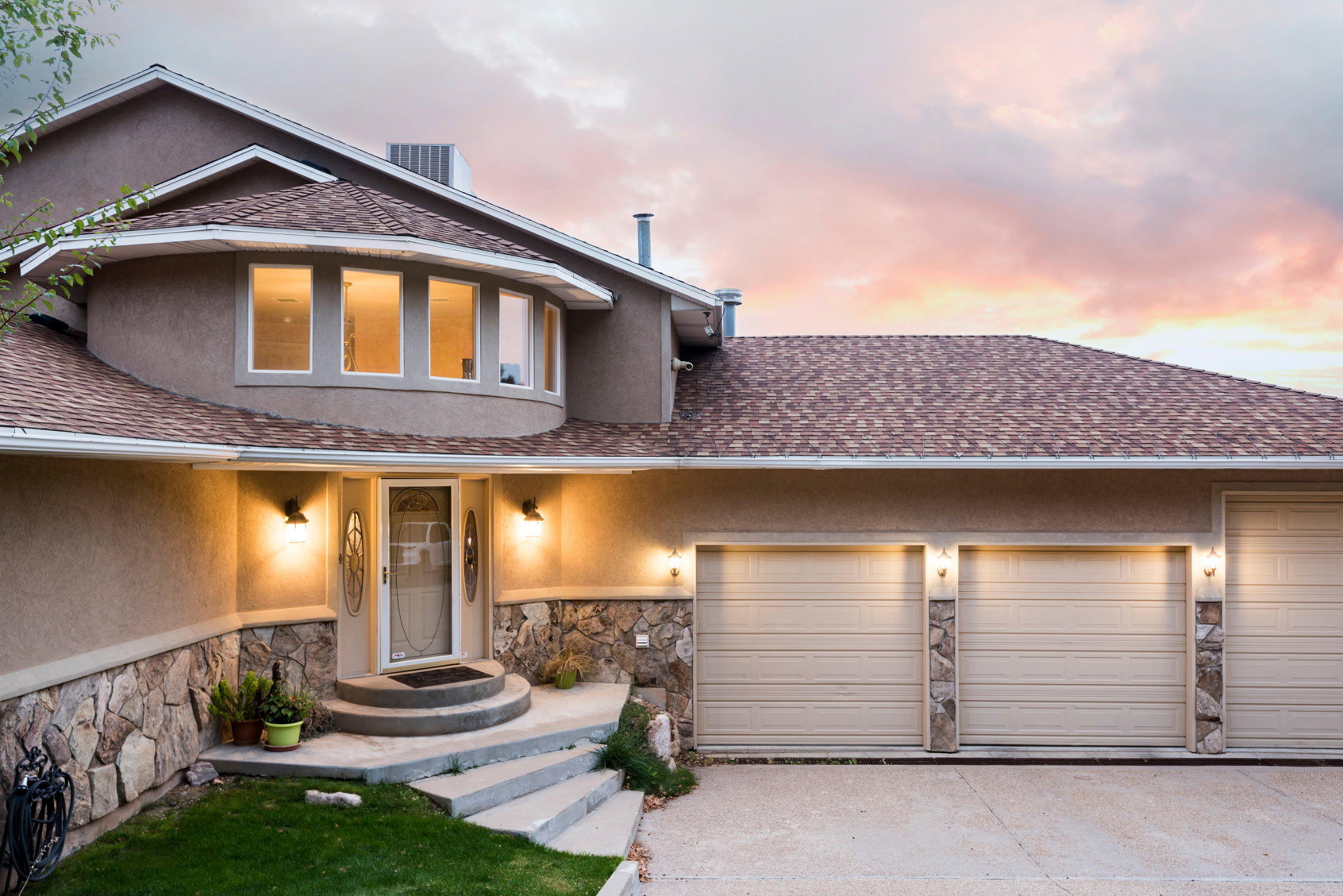 Stucco exterior featuring a stone accent foundation and a multi-level asphalt shingle roof