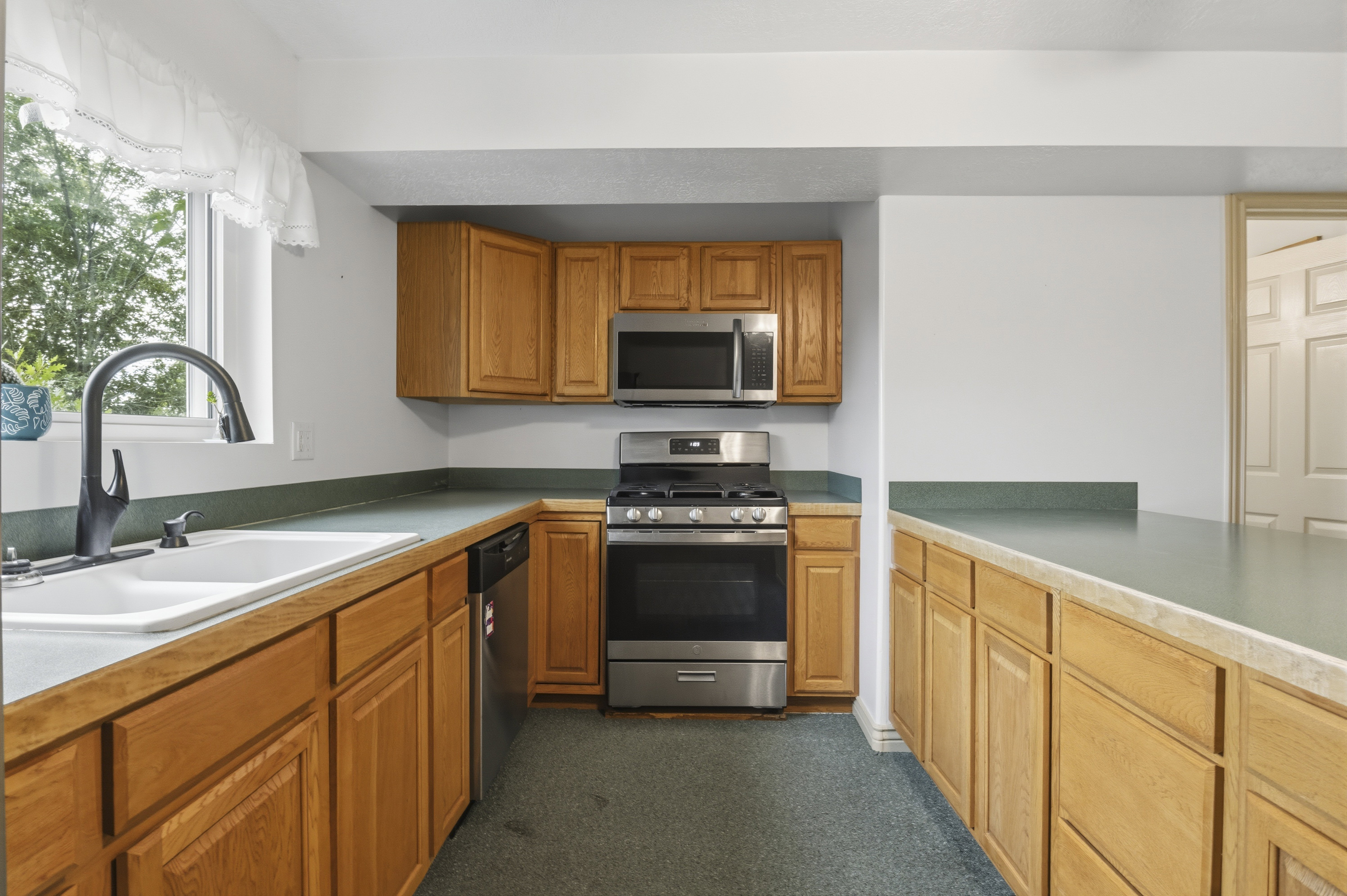 Kitchen featuring natural wood cabinetry, light green countertops, stainless steel appliances, and a window above the sink