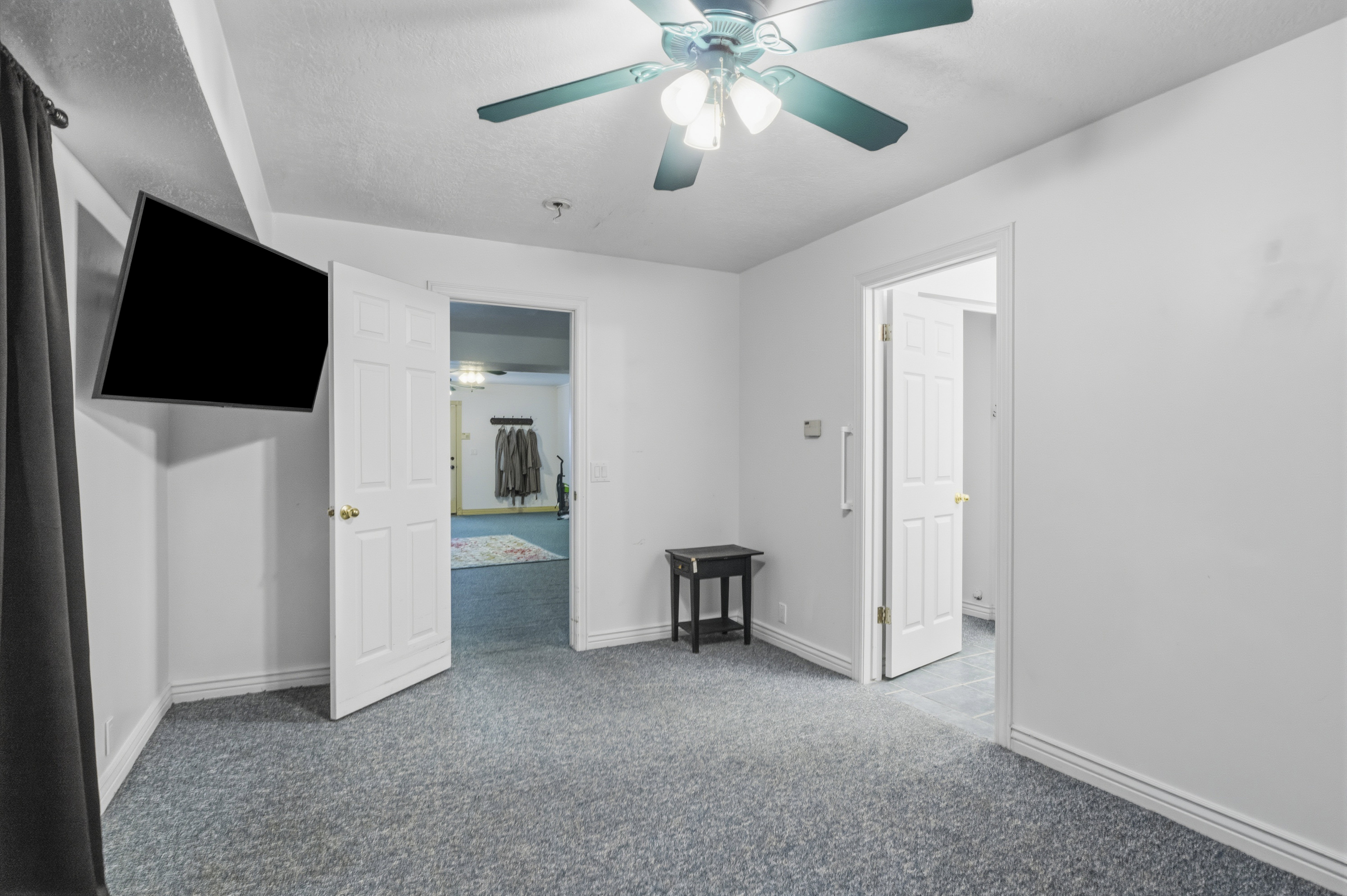 Carpeted room featuring a ceiling fan with integrated lighting, white walls, and two white paneled doors