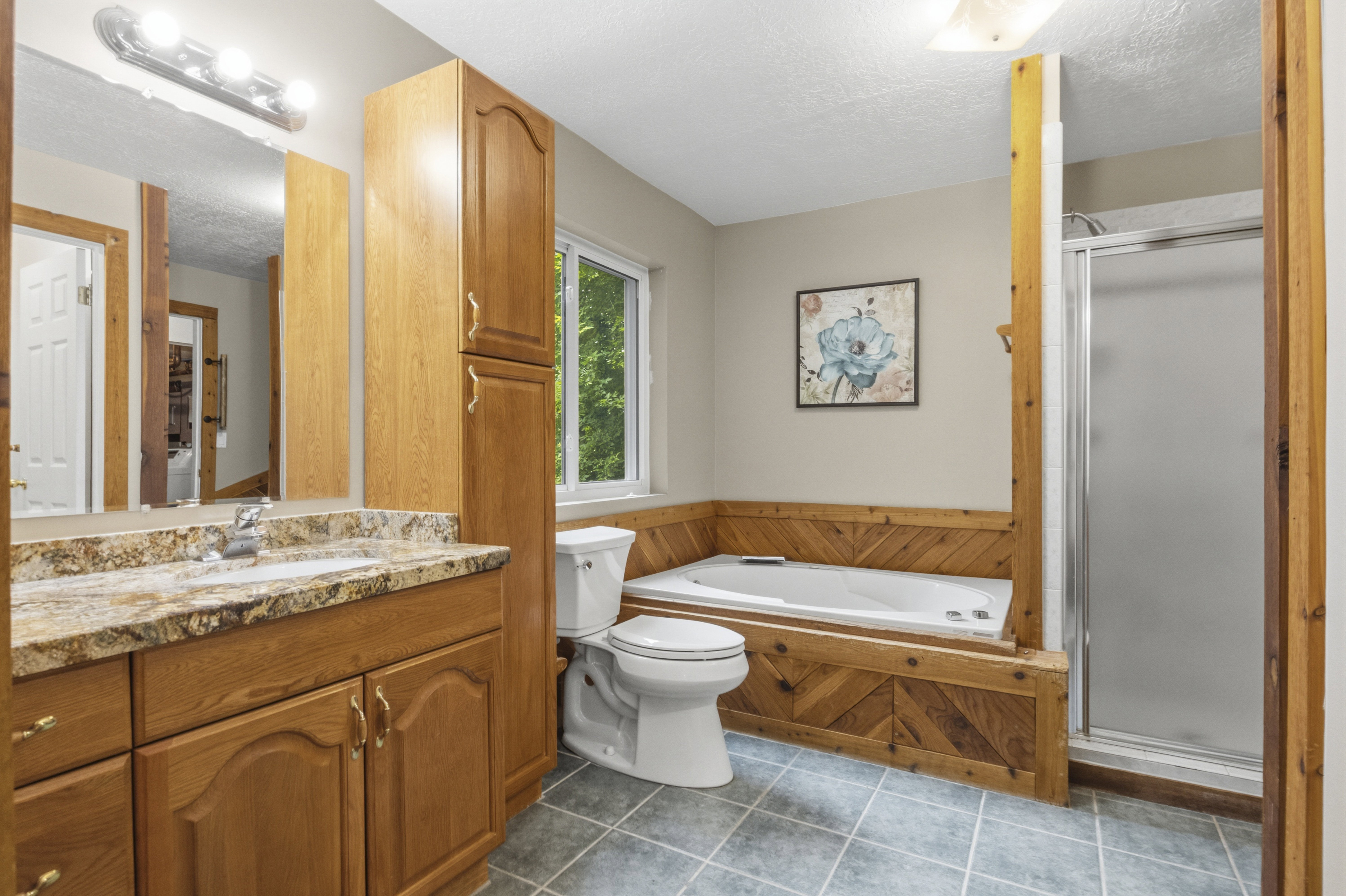 Bathroom featuring a built-in jetted tub, a separate glass-enclosed shower, a vanity with a stone-finish countertop, and wood cabinetry